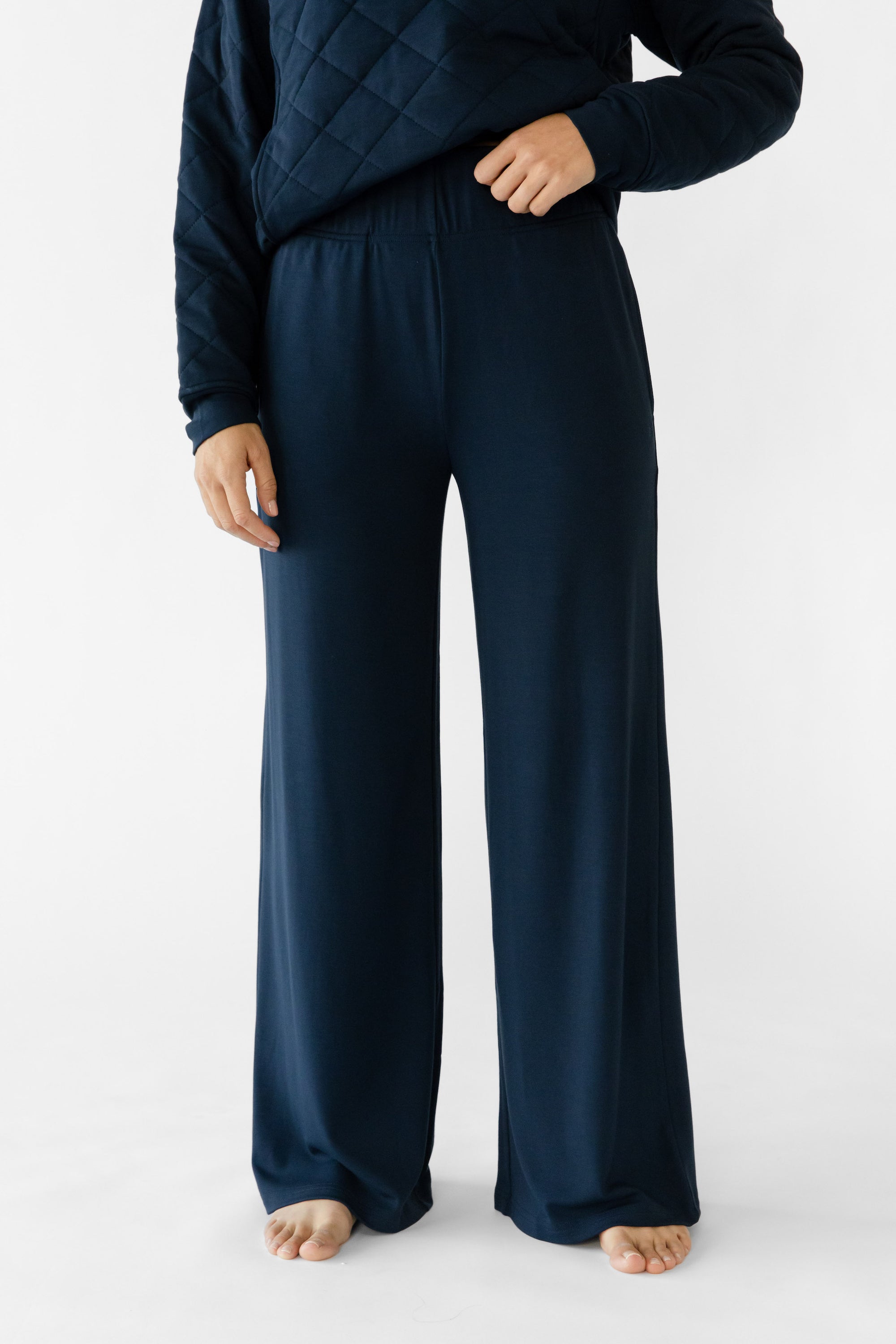 A woman stands in a relaxed pose wearing navy lounge pants set from Cozy Earth, featuring the Women's Ultra-Soft Bamboo Wide Leg Pull On Pant TALL. 