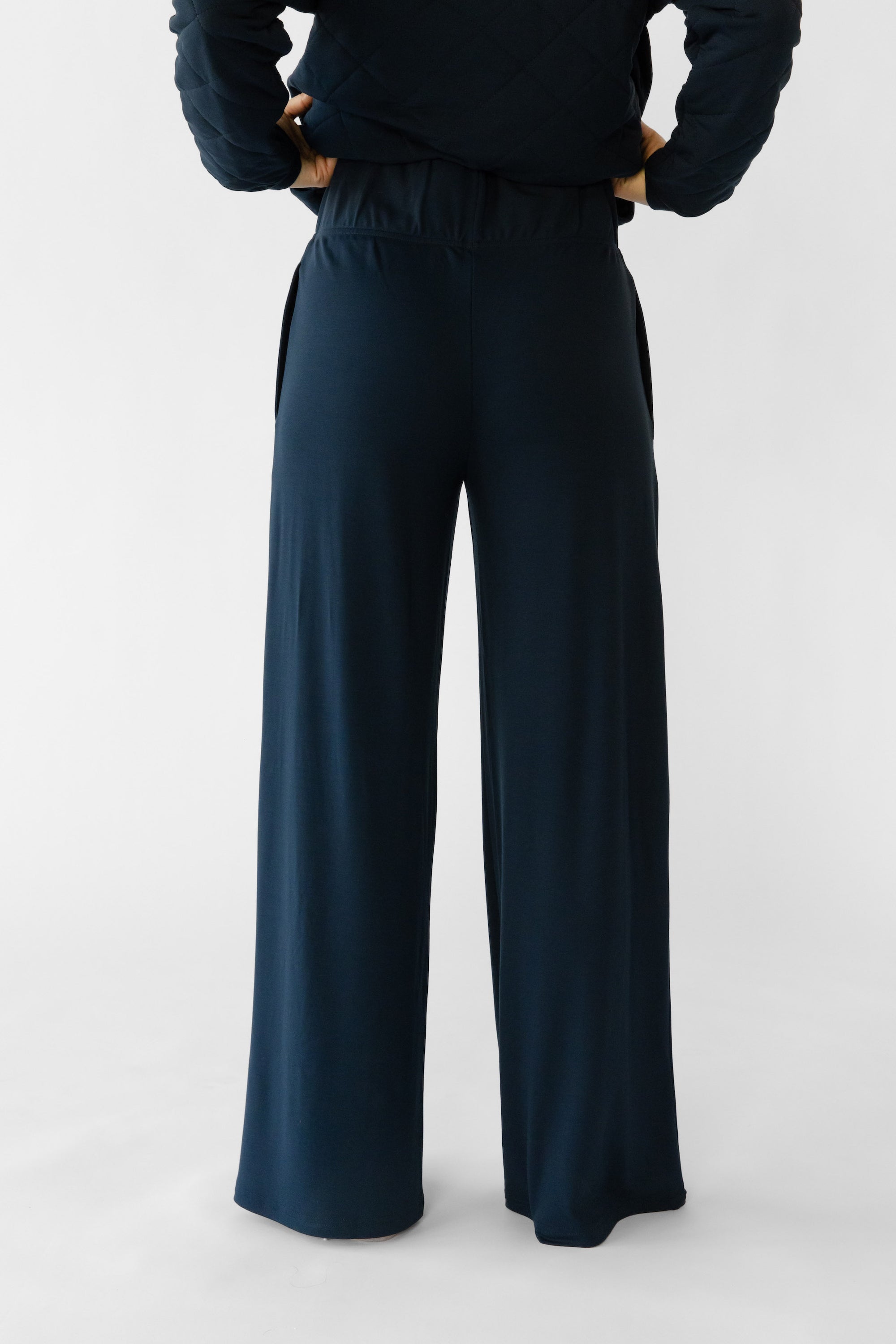 A woman stands in a relaxed pose wearing navy lounge pants set from Cozy Earth, featuring the Women's Ultra-Soft Bamboo Wide Leg Pull On Pant TALL. 