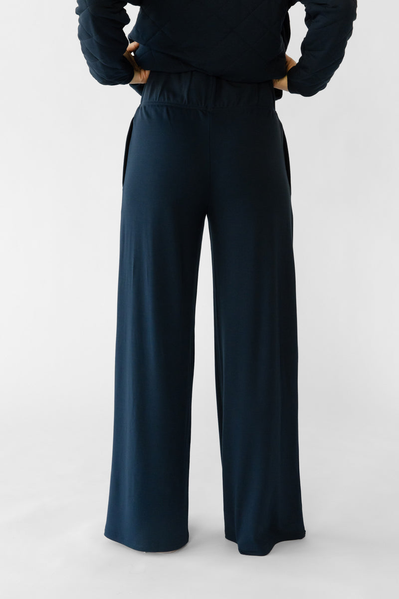 A woman stands in a relaxed pose wearing navy lounge pants set from Cozy Earth, featuring the Women's Ultra-Soft Bamboo Wide Leg Pull On Pant TALL.