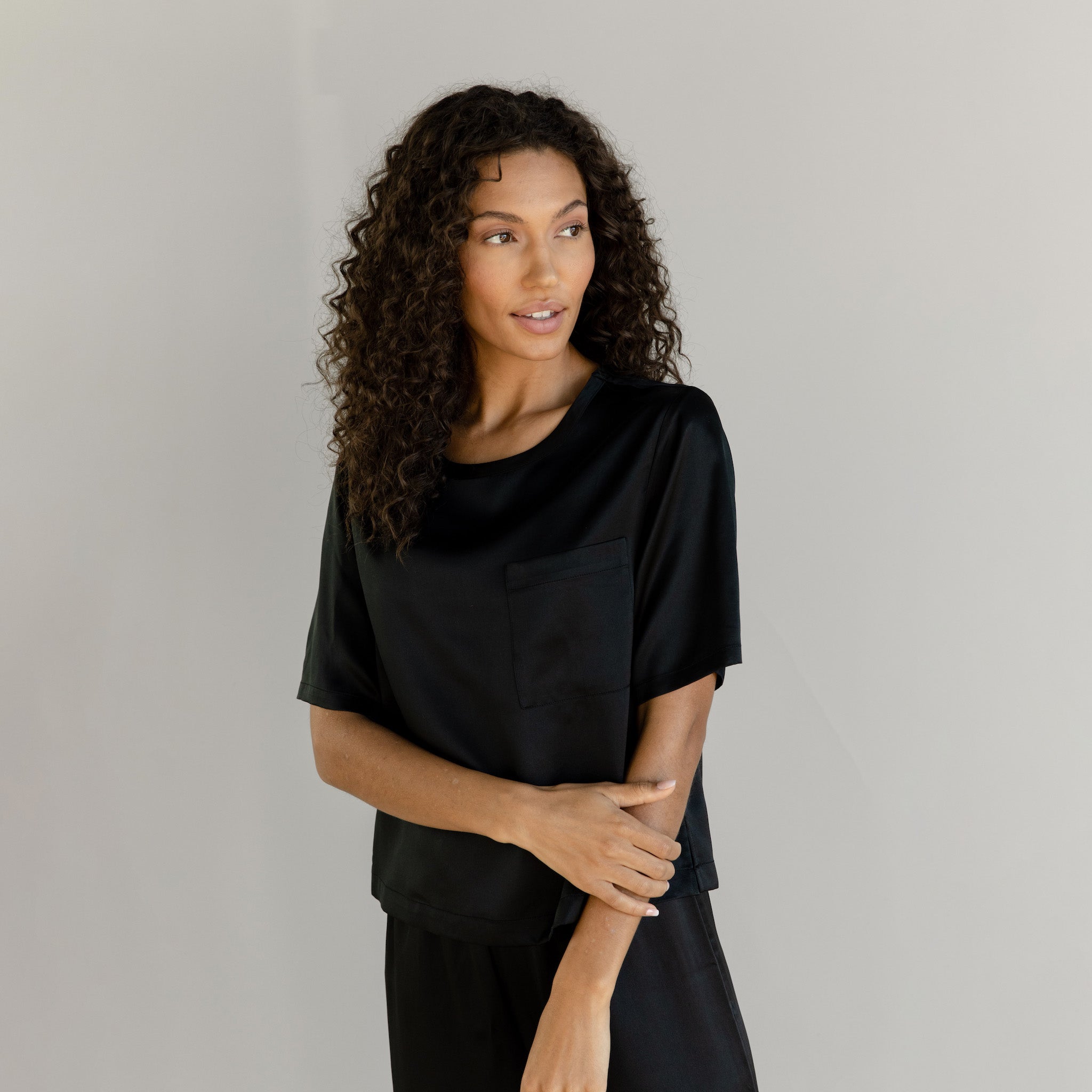 Black Serenity Silk Scoop Neck Tee modeled by a woman. The photo was taken in a high contrast setting, showing off the colors and lines of the tee. |Color: Black