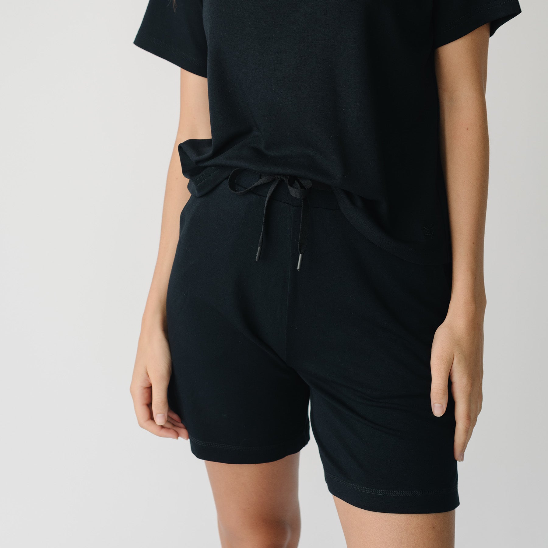 Woman wearing a black t-shirt and black Cozy Earth Brushed Bamboo Mid-Length Shorts shorts on a plain background 
