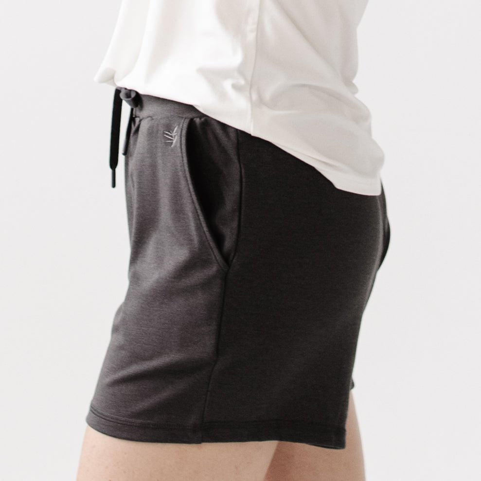 Person turned to the side wearing Cozy Earth Brushed Bamboo Jogger Shorts in dark grey and a white top on a light background 