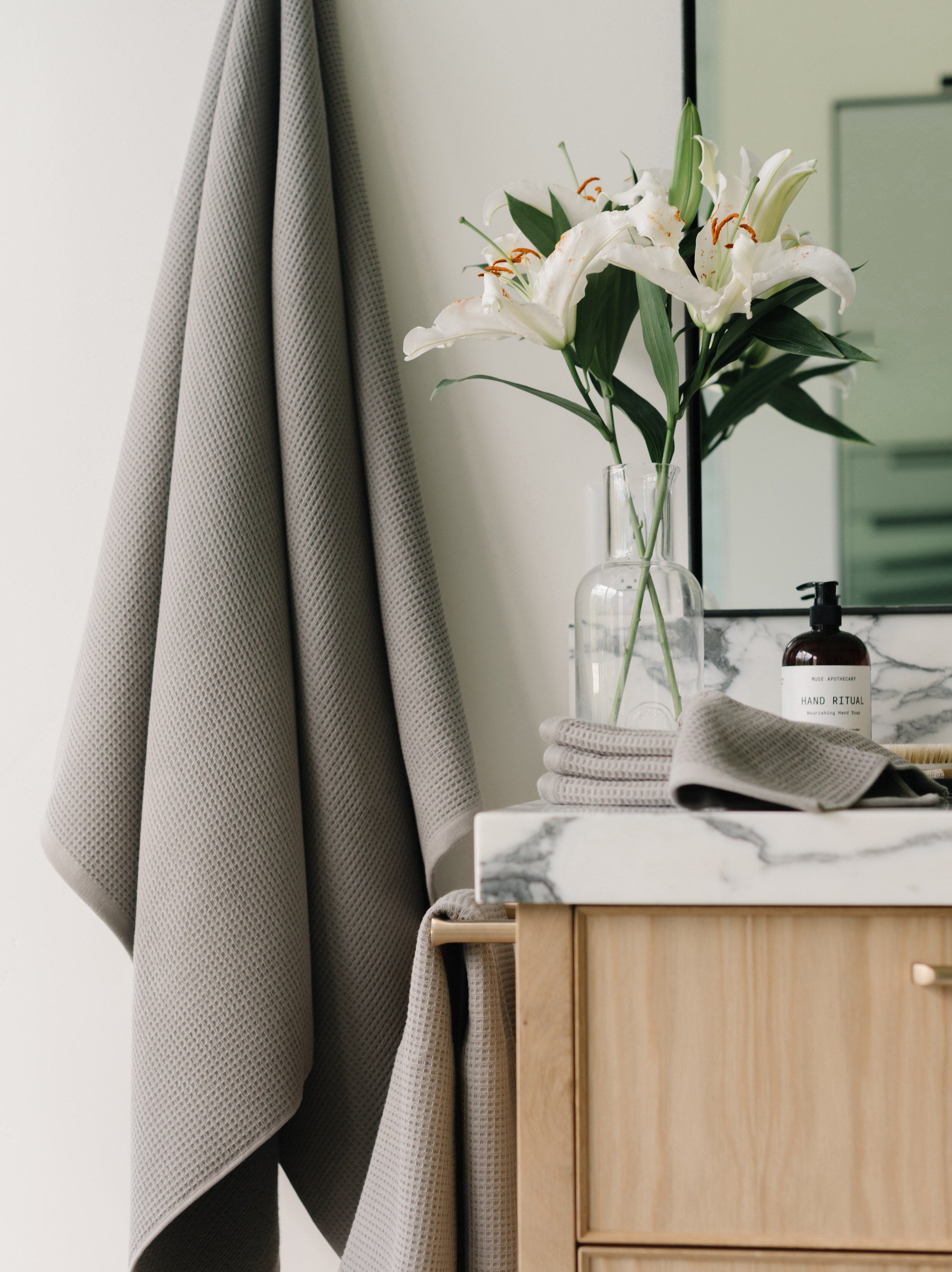 Waffle Bath Towel in the color Charcoal. Photo of Charcoal Waffle Bath Towel taken with Charcoal Waffle Bath Towel hanging from towel hook in a bathroom with white walls |Color:Charcoal