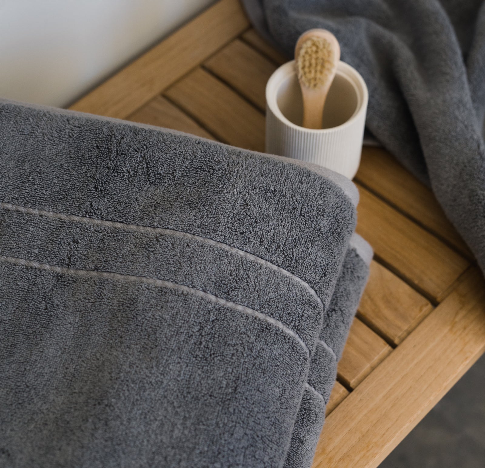The Premium Plush Bath Sheet are folded on a wooden bench. Bath products are resting on the bench as well. 
