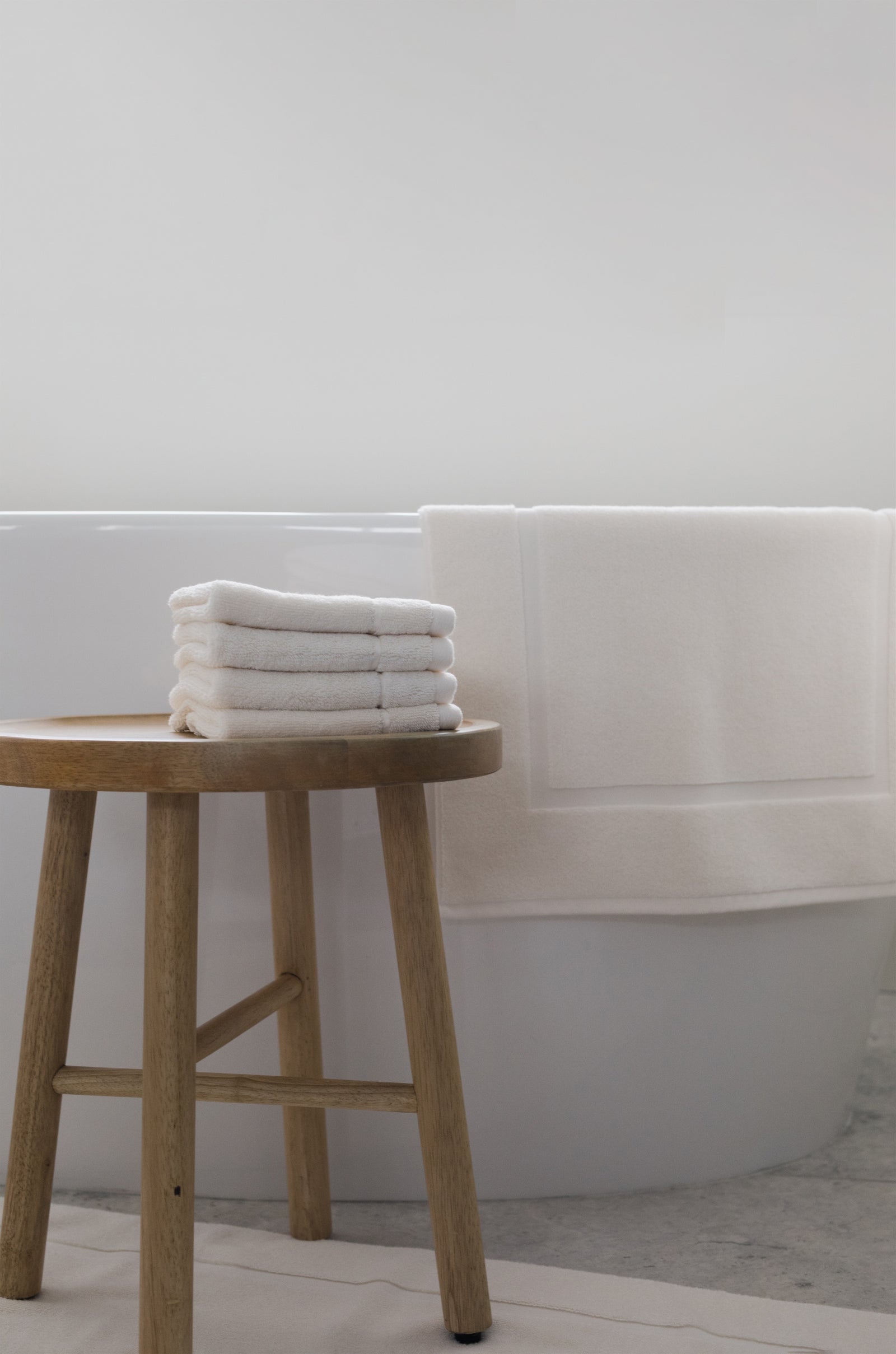 Creme Premium Plush Bath Mat resting on white bathtub. The photo was taken in a bathroom showing a wooden stool with wash cloths next to the bathtub.