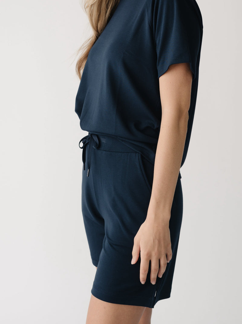 Woman wearing a navy t-shirt and navy Cozy Earth Brushed Bamboo Mid-Length Shorts shorts on a plain background