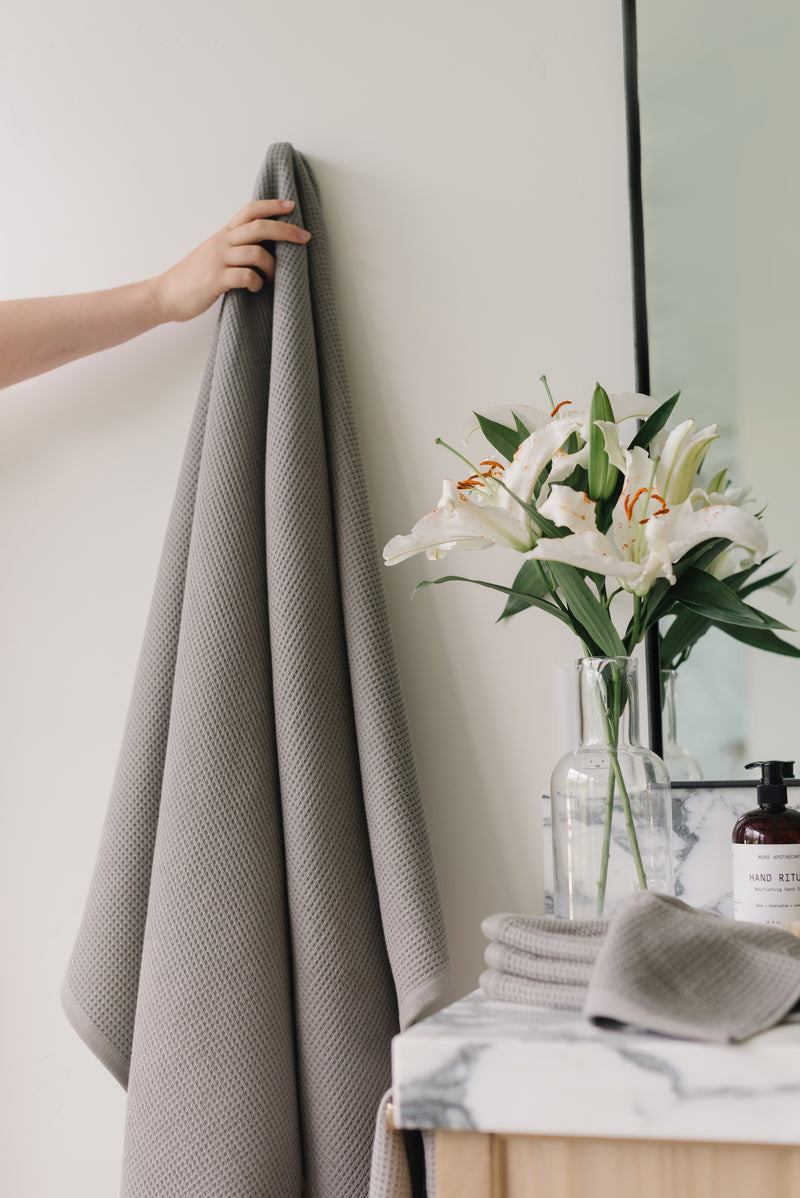 Waffle Bath Towel in the color Charcoal. Photo of Charcoal Waffle Bath Towel taken with Charcoal Waffle Bath Towel hanging from towel hook in a bathroom with white walls