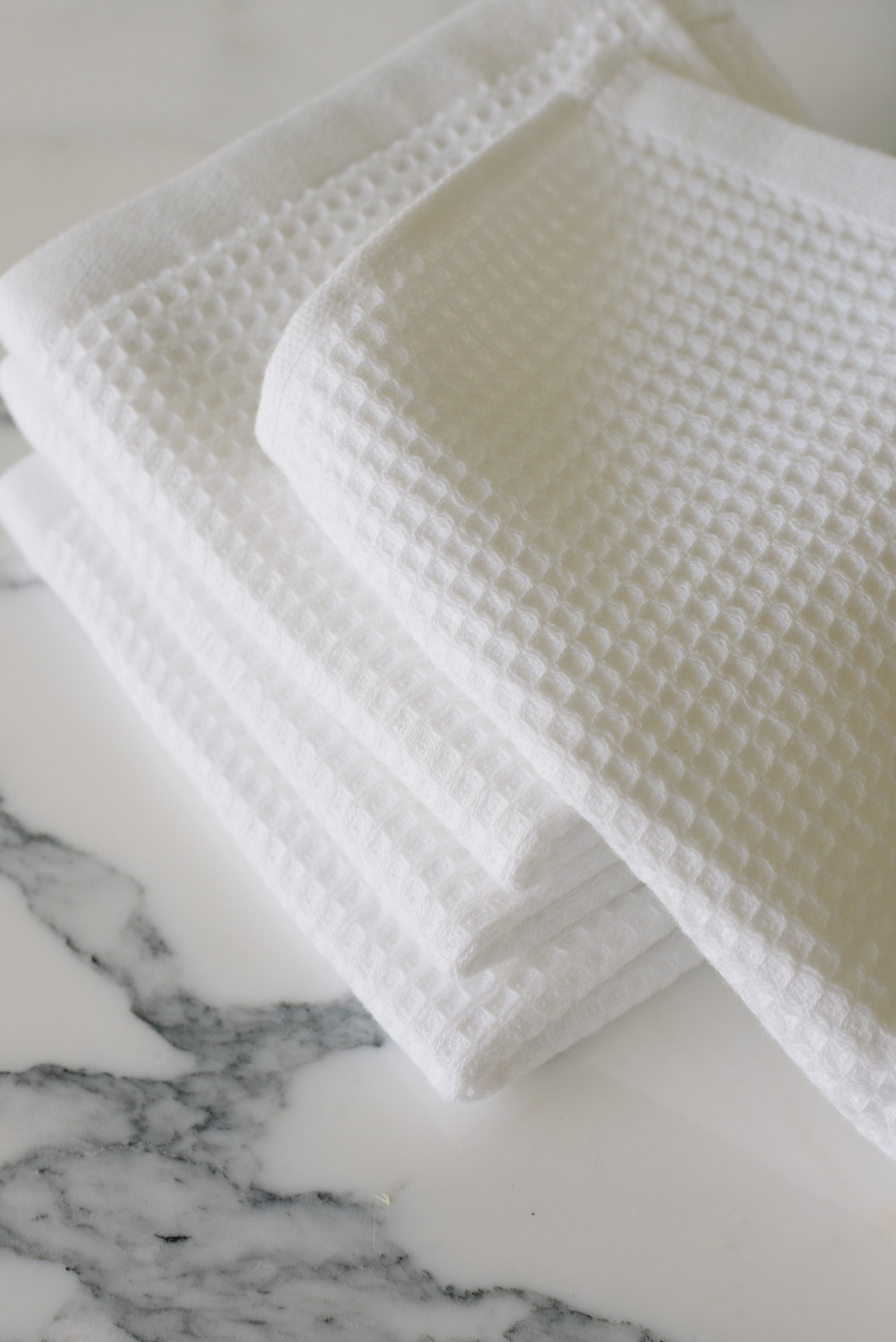 White Waffle Wash Cloths neatly folded. The photo was taken with the cloths resting on a white marble sink. 