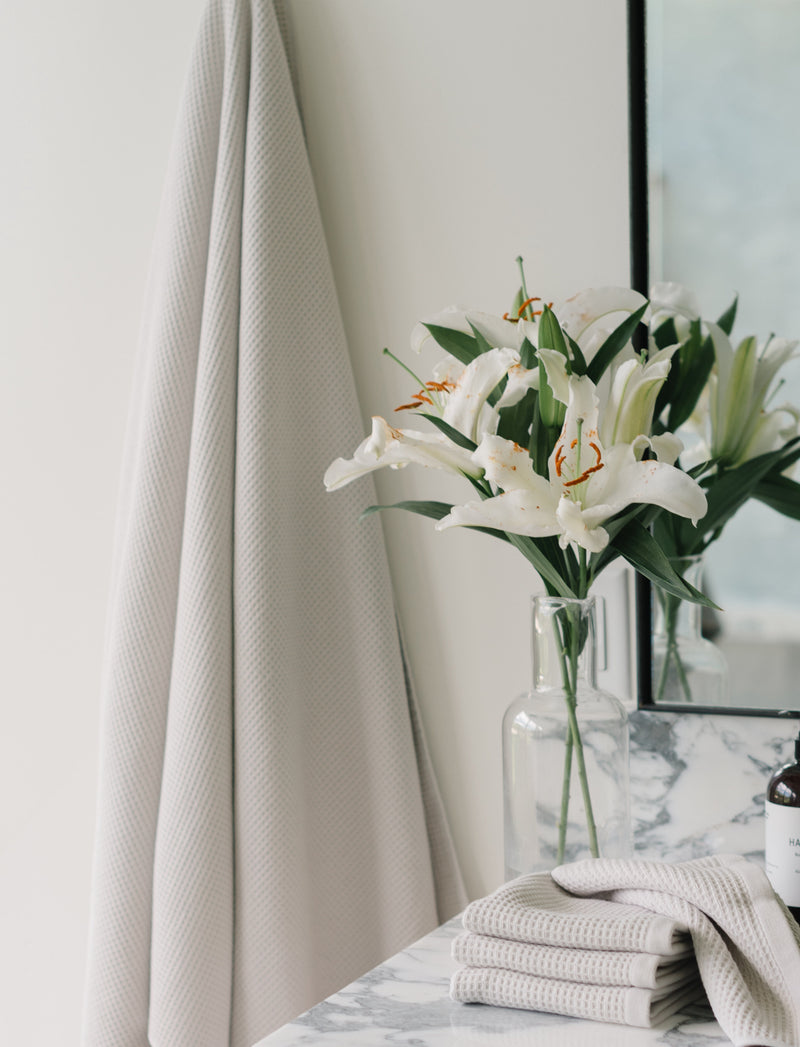 Waffle Wash Clothes in the color Light Grey. Photo of Light Grey Waffle Wash Clothes taken in a bathroom with the Waffle Wash Clothes resting on a bathroom sink.