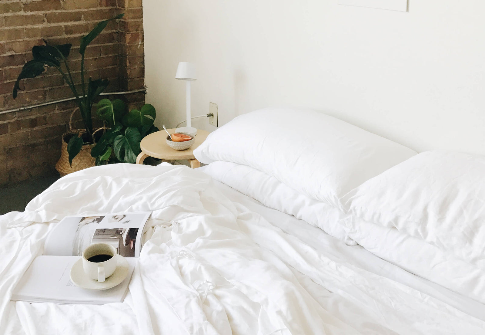 Bed with white bedding, standard/king pillows, and a cup of coffee and magazine on top