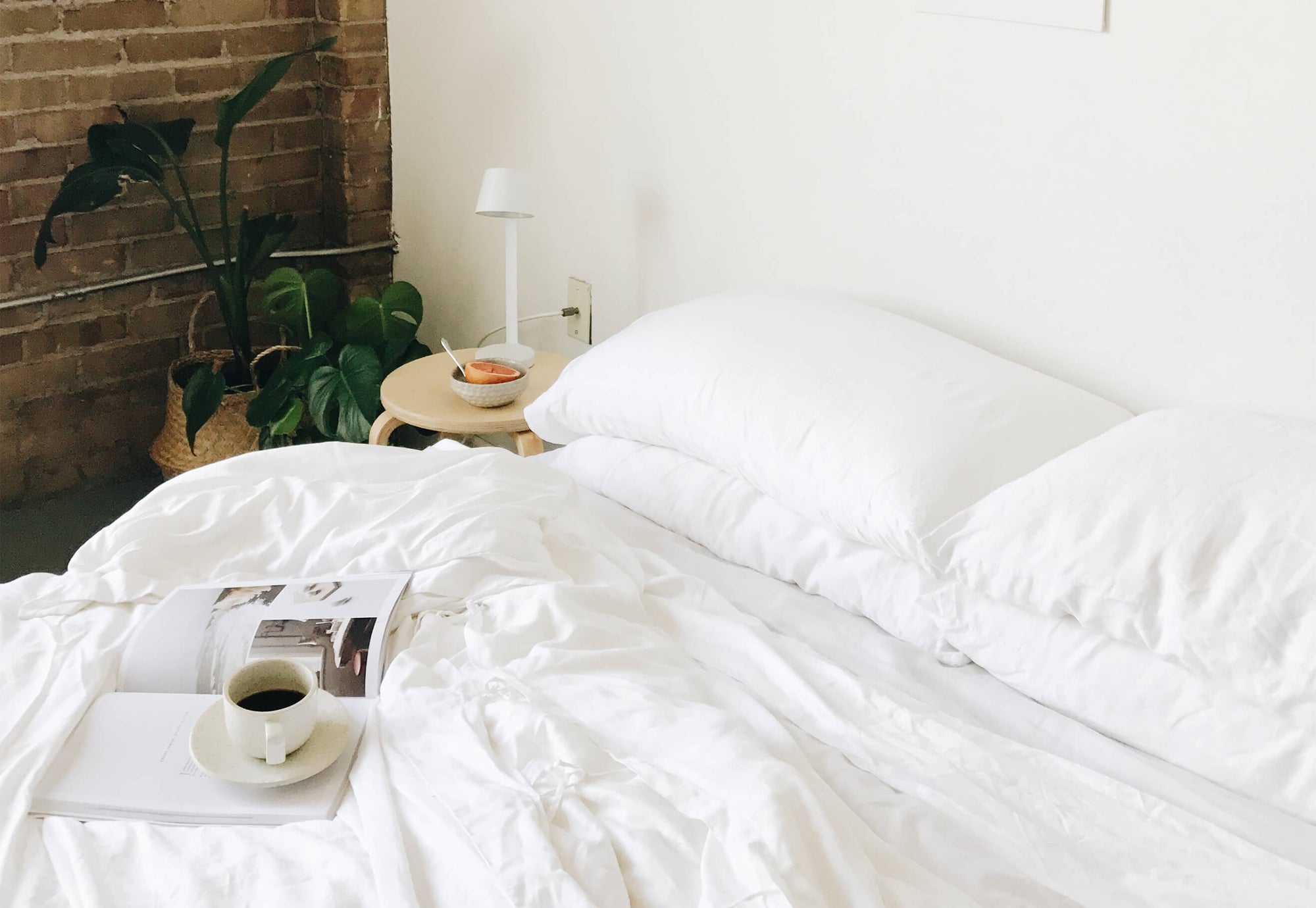 Bed with white bedding, standard/king pillows, and a mug and magazine on top 