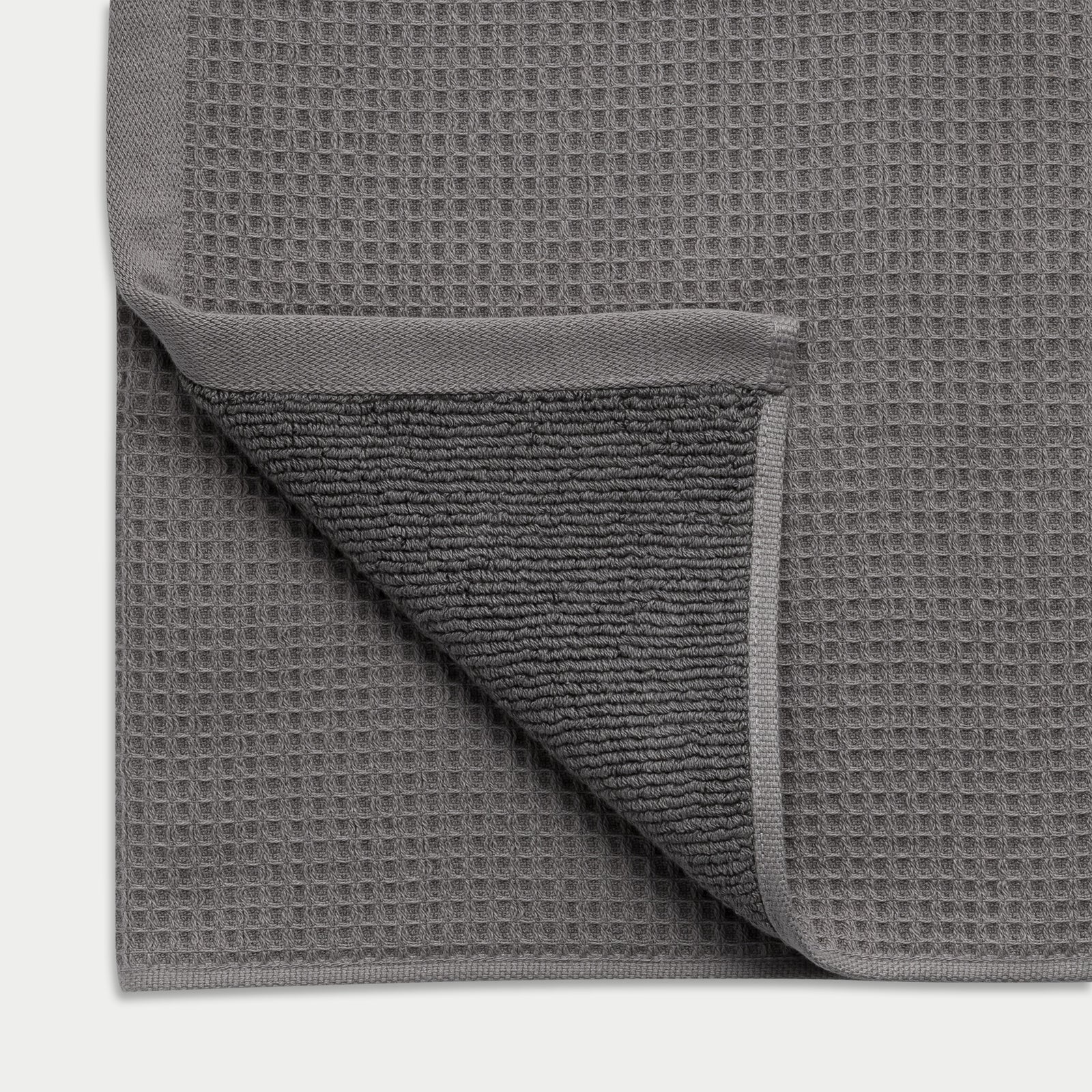 Charcoal Waffle Hand Towel resting flat on a white background. The corner is folded so that both sides of the towel can be seen. 