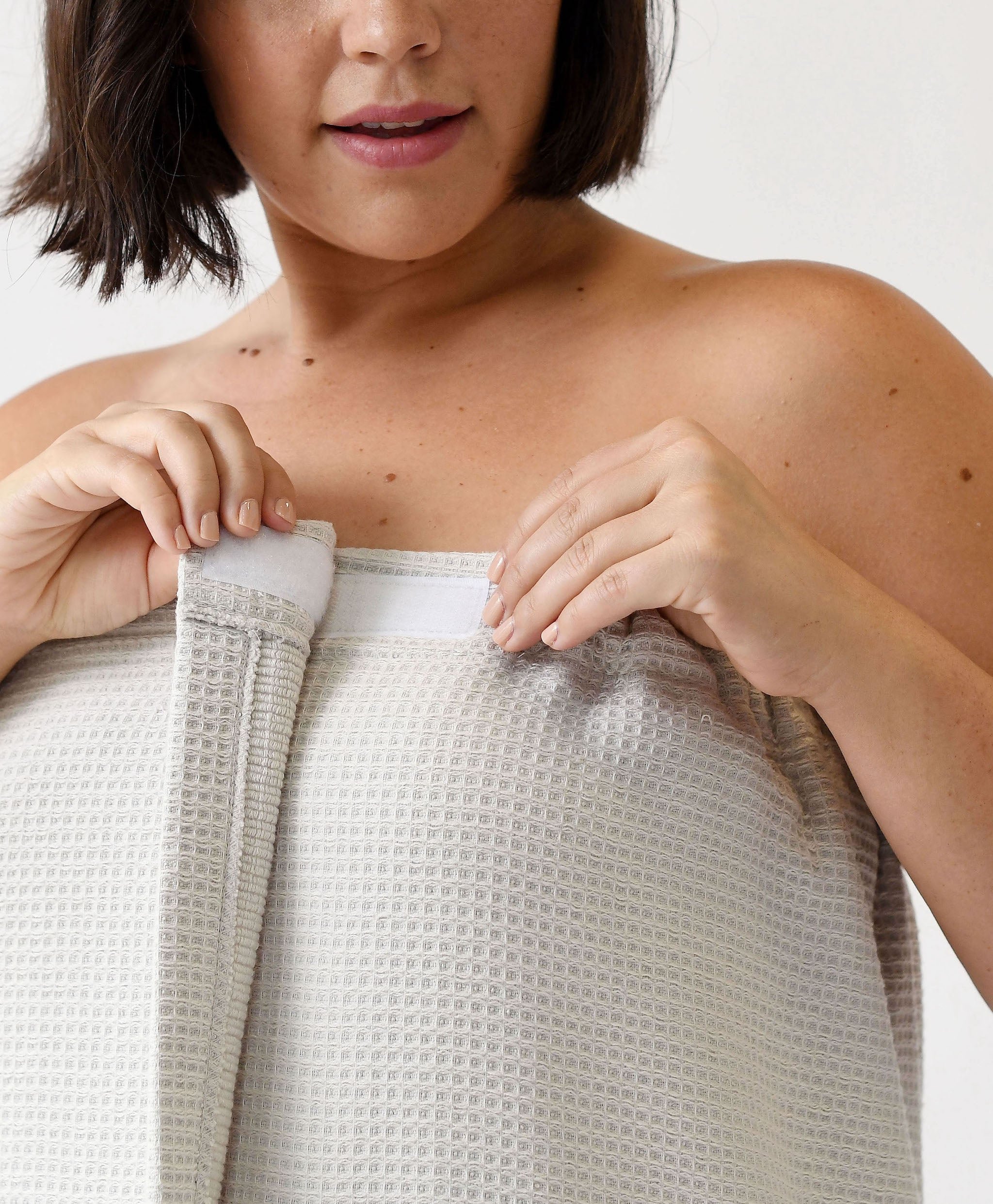 Light Grey Waffle Bath Wrap. The bath wrap is shown being worn by a woman. Photo was taken with a white background.
