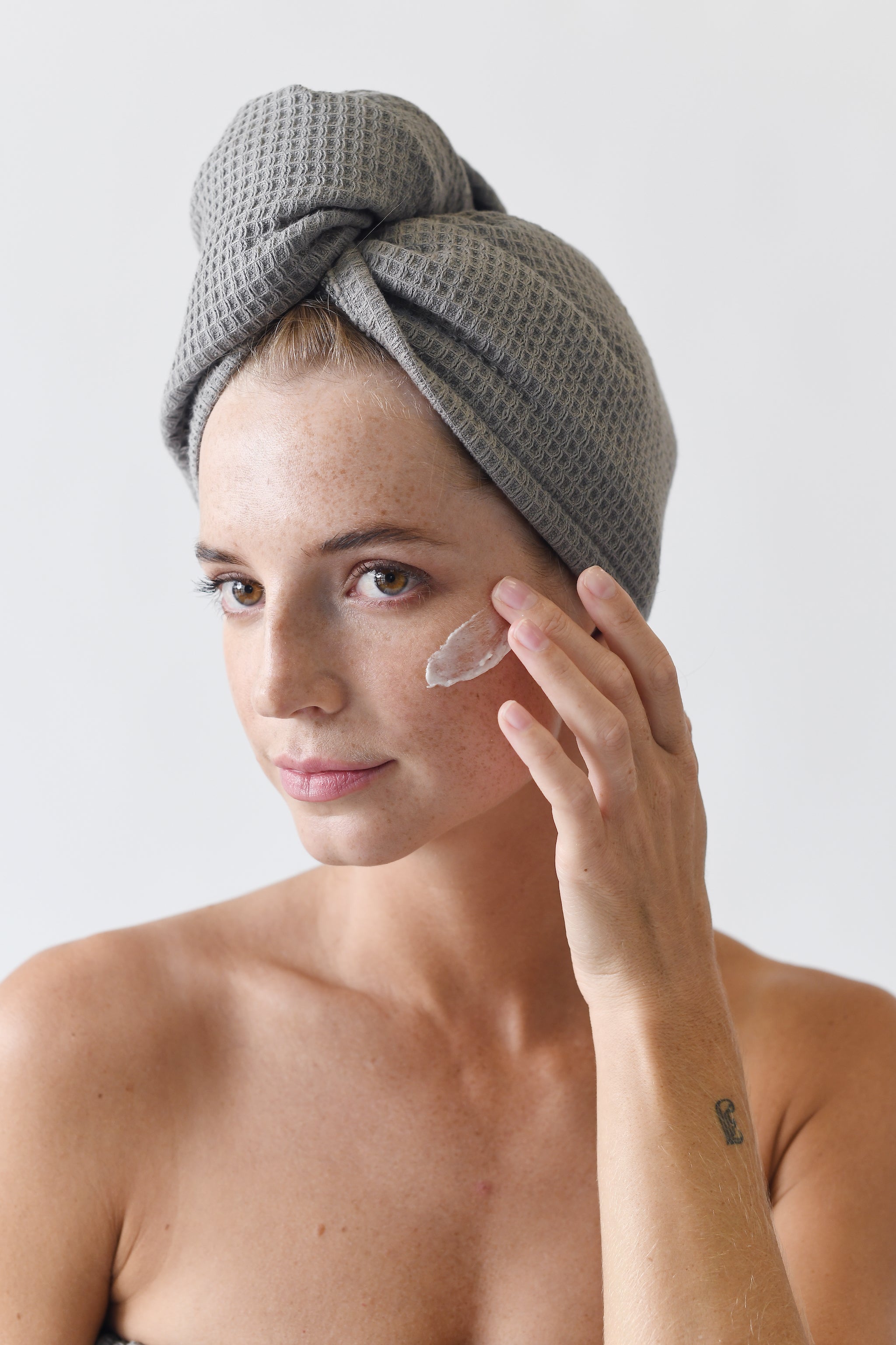 Charcoal Waffle Hair Towel. The hair towel is shown being worn by a woman who is applying a facial cream. |Color:Charcoal