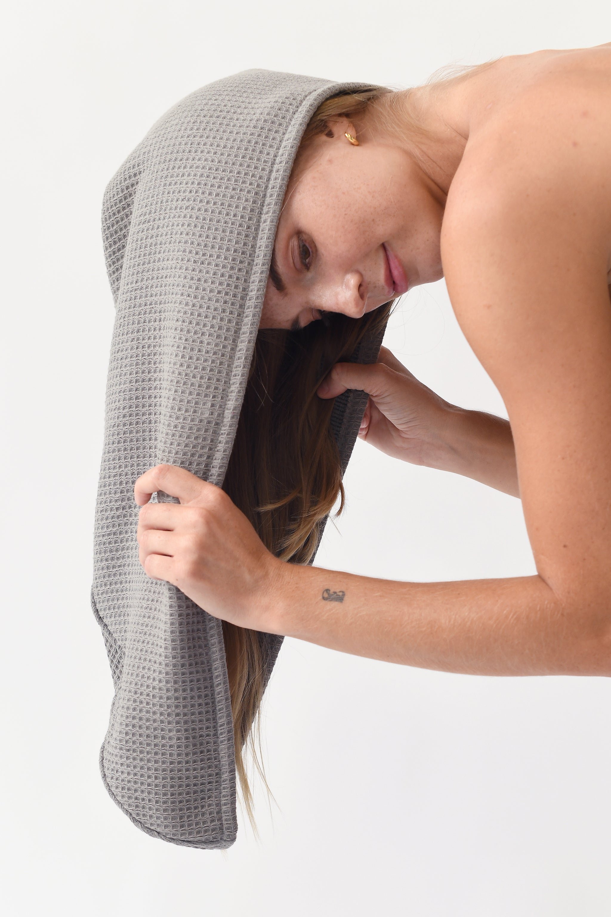 Charcoal Waffle Hair Towel. The hair towel is shown being worn by a woman who is in the early steps of putting on the hair towel. 