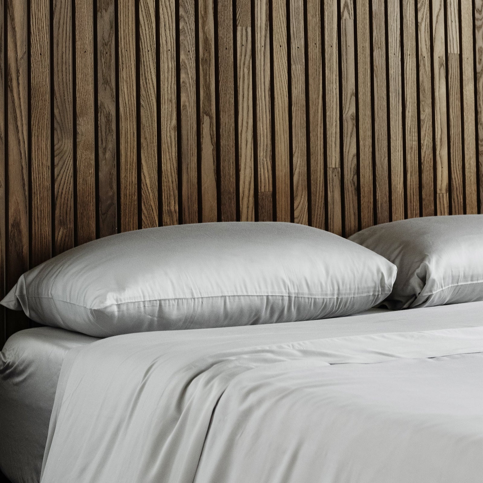 Bed with light grey bedding and wooden walls 