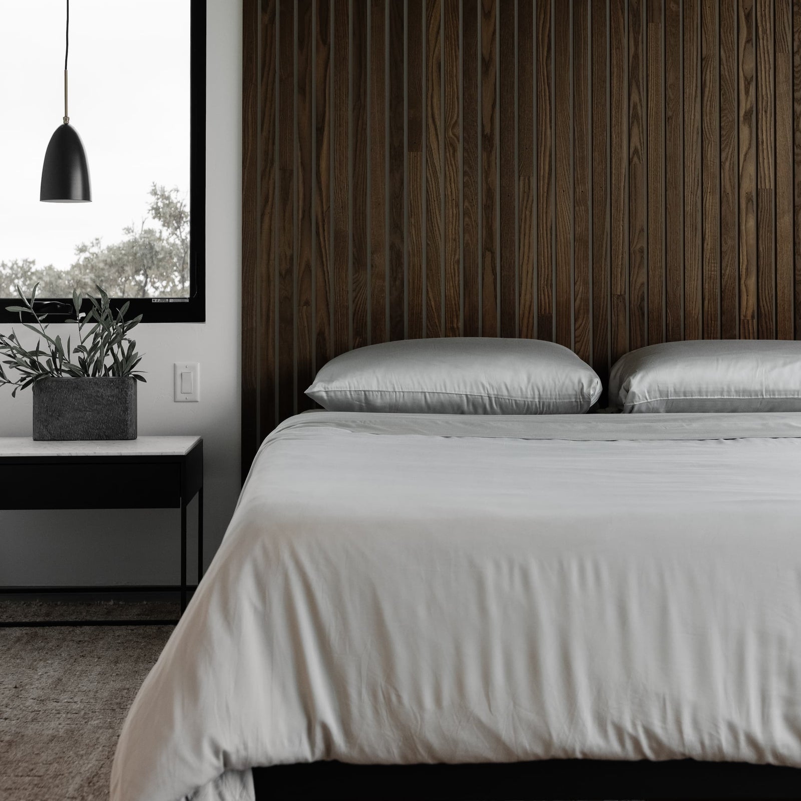 Bedroom with dark wood walls and bed with light grey bedding 