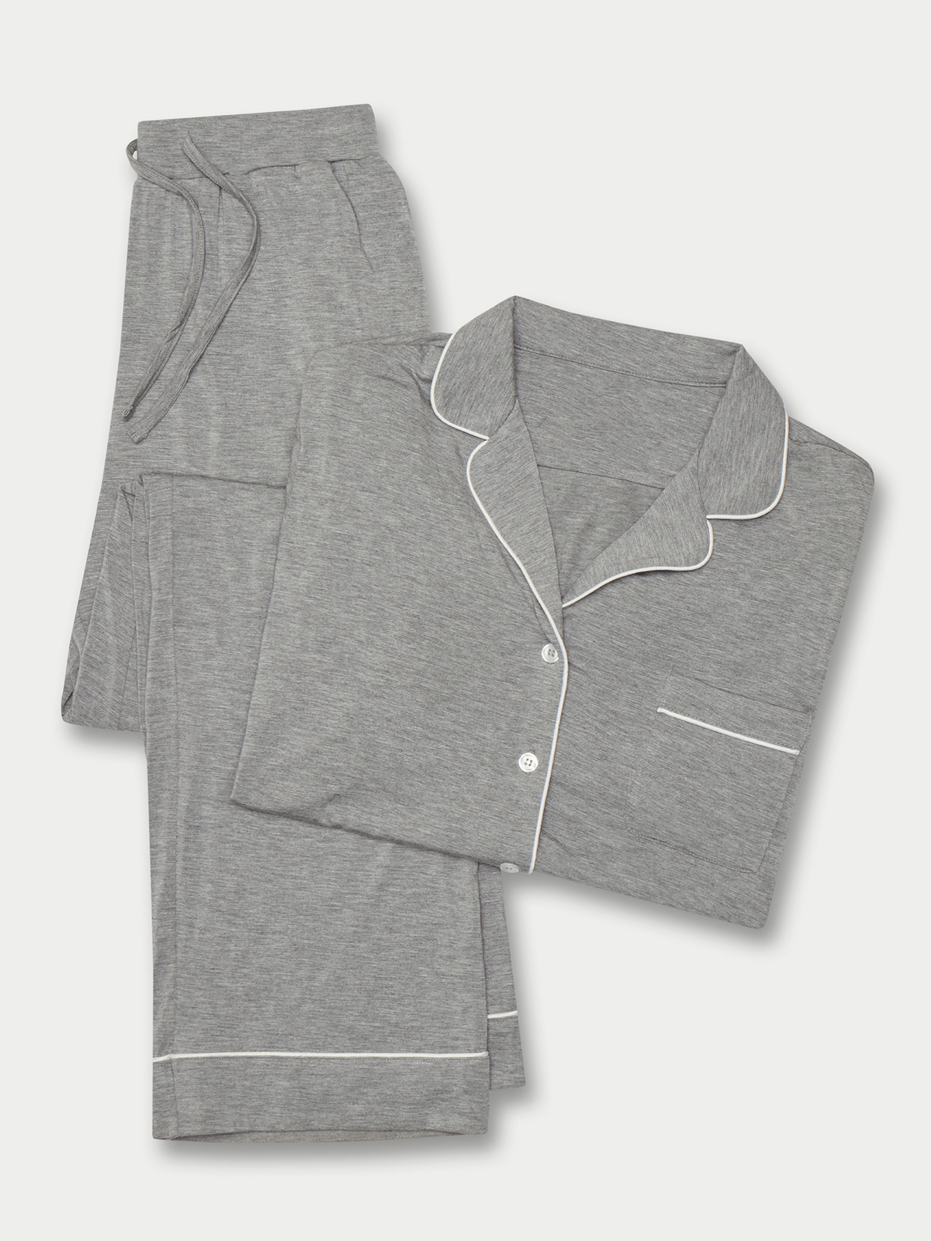 A neatly folded set of Women's Stretch-Knit Long Sleeve Bamboo Pajamas in PETITE by Cozy Earth, featuring a gray color with white piping. The set includes a button-up long-sleeved shirt with a chest pocket and matching pants with an elastic drawstring waist. The fabric appears soft and comfortable. The items are laid out against a plain background.