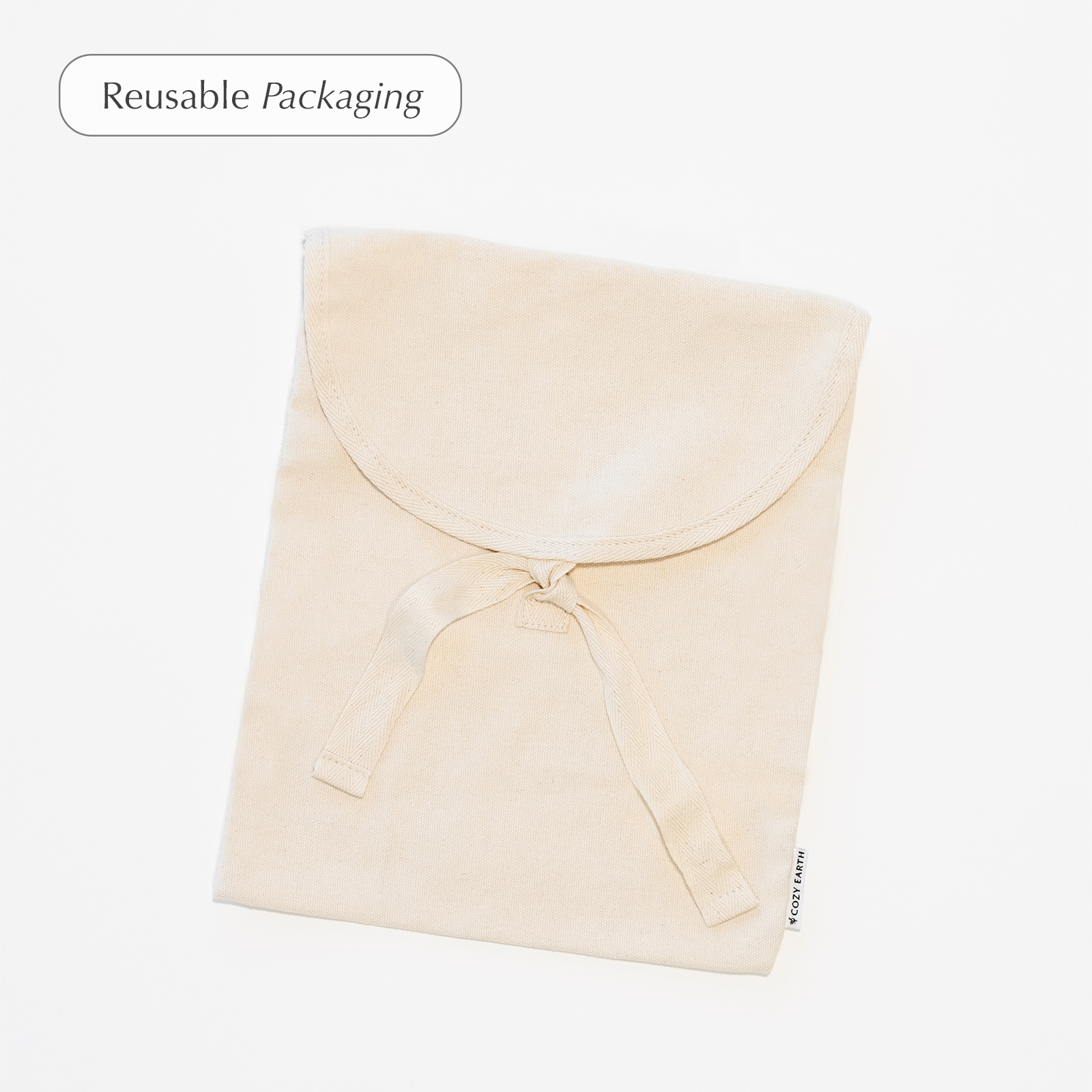 A beige fabric bag with a flap top tied with two fabric straps is shown against a white background, featuring a small label attached to its edge. A text overlay in the top left corner reads "Reusable Packaging" from the Bamboo Pillowcases by Cozy Earth.