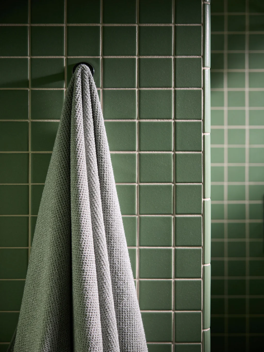 Gray towel hanging on a wall with green tiles.