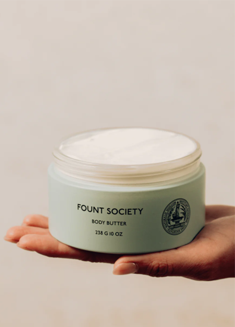 A hand holding a jar of Fount Society body butter.