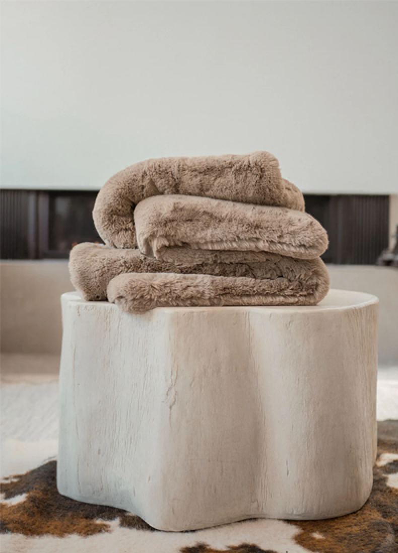 Soft beige blankets folded on a tree-stump style table.