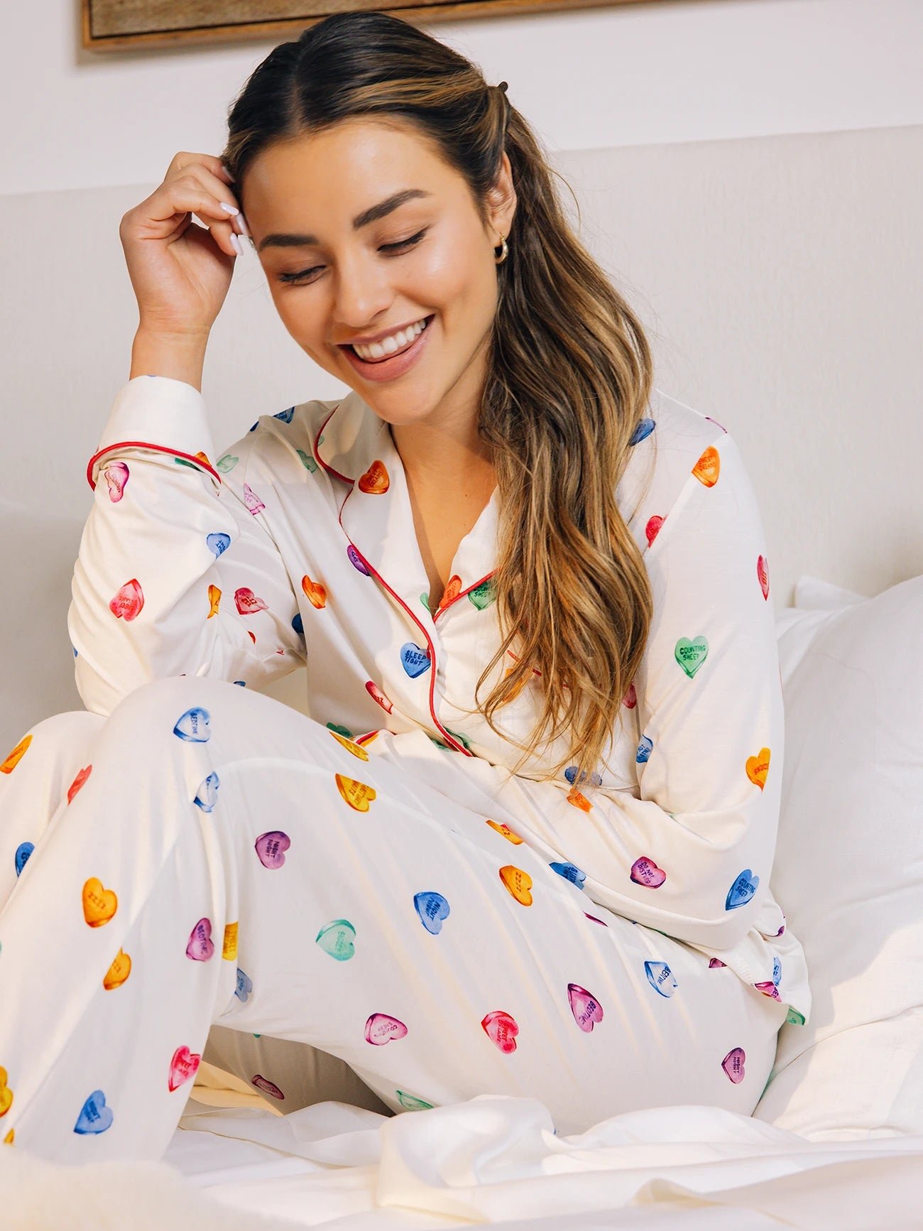 Person smiling in colorful heart-patterned pajamas sitting on a bed.