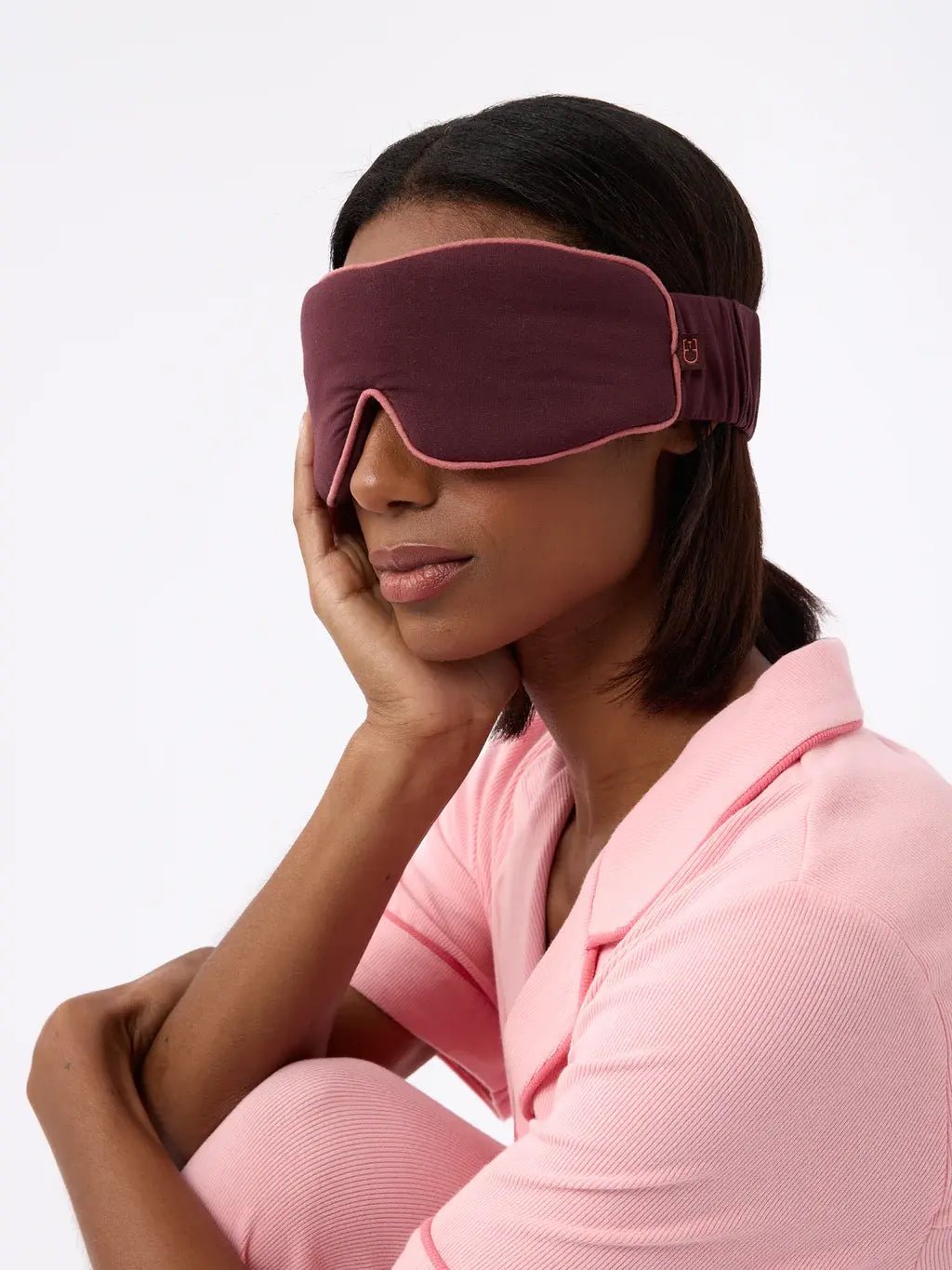 Person wearing a pink sleep mask and pajamas, resting their head on their hand.