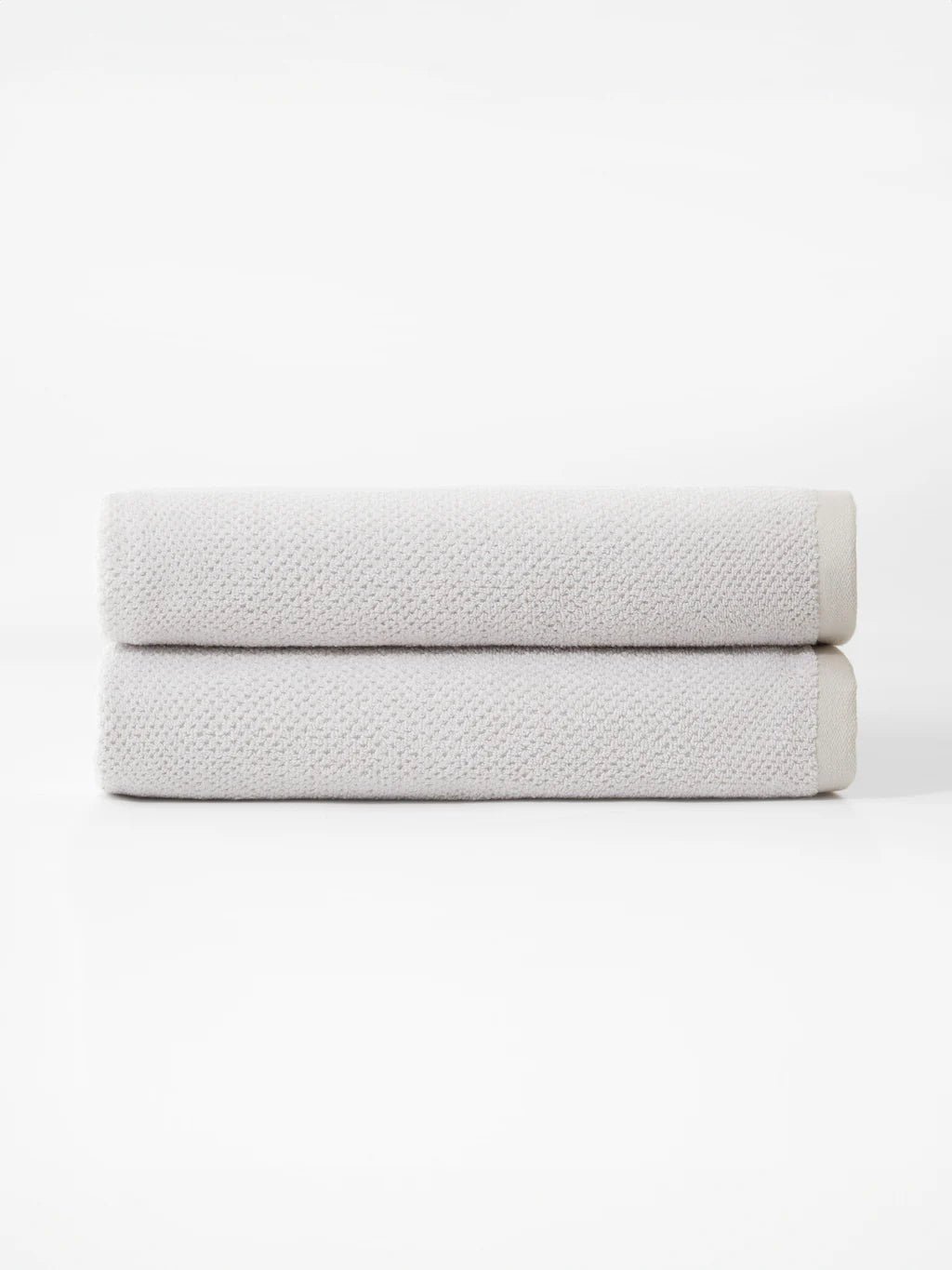 Two folded light gray towels stacked on a plain white surface.