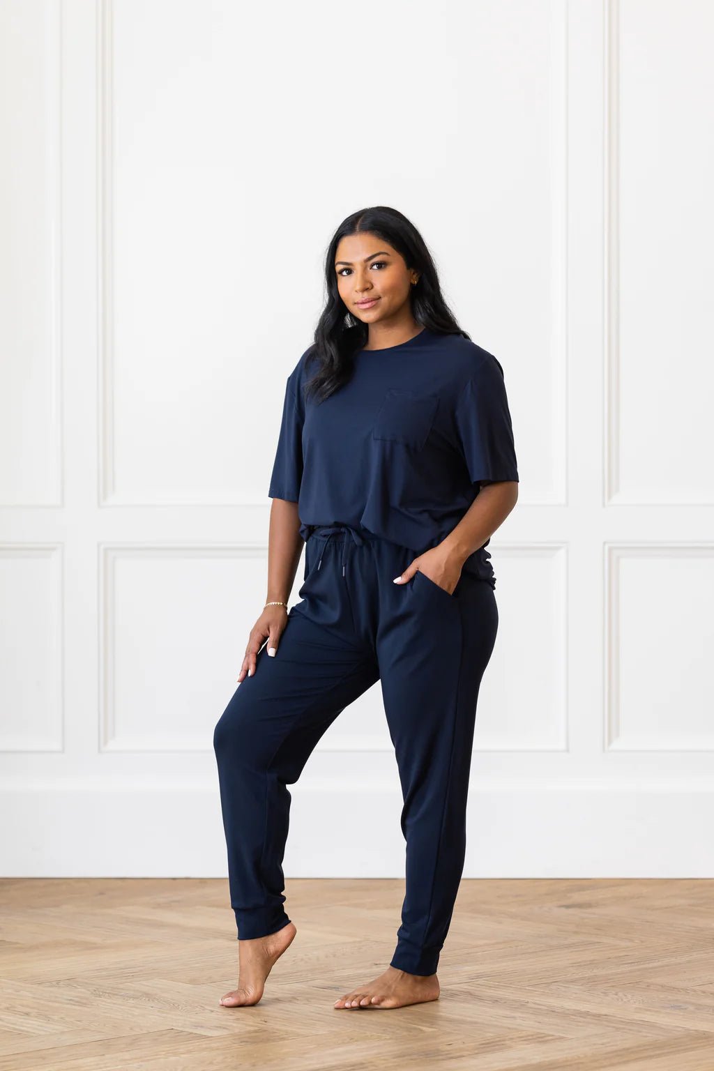 A woman in a dark blue loungewear set poses in a bright, minimalistic room.