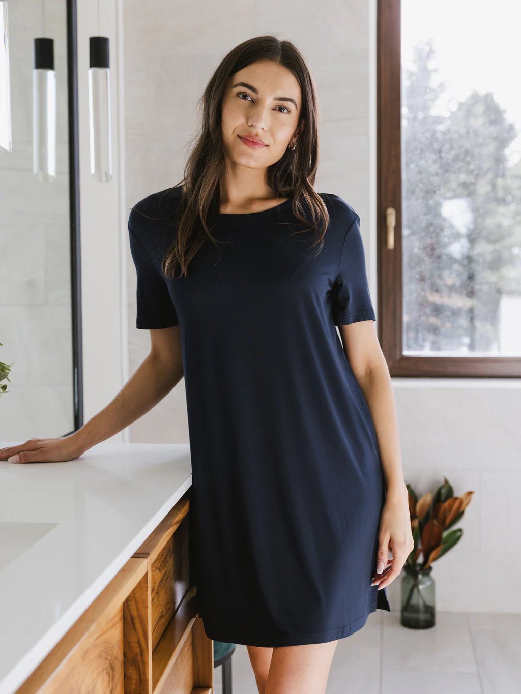 Woman in a navy dress standing by a bathroom counter.