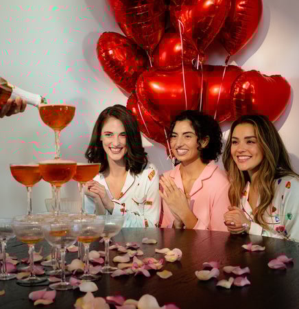 Three women celebrating with champagne glasses and red heart balloons.