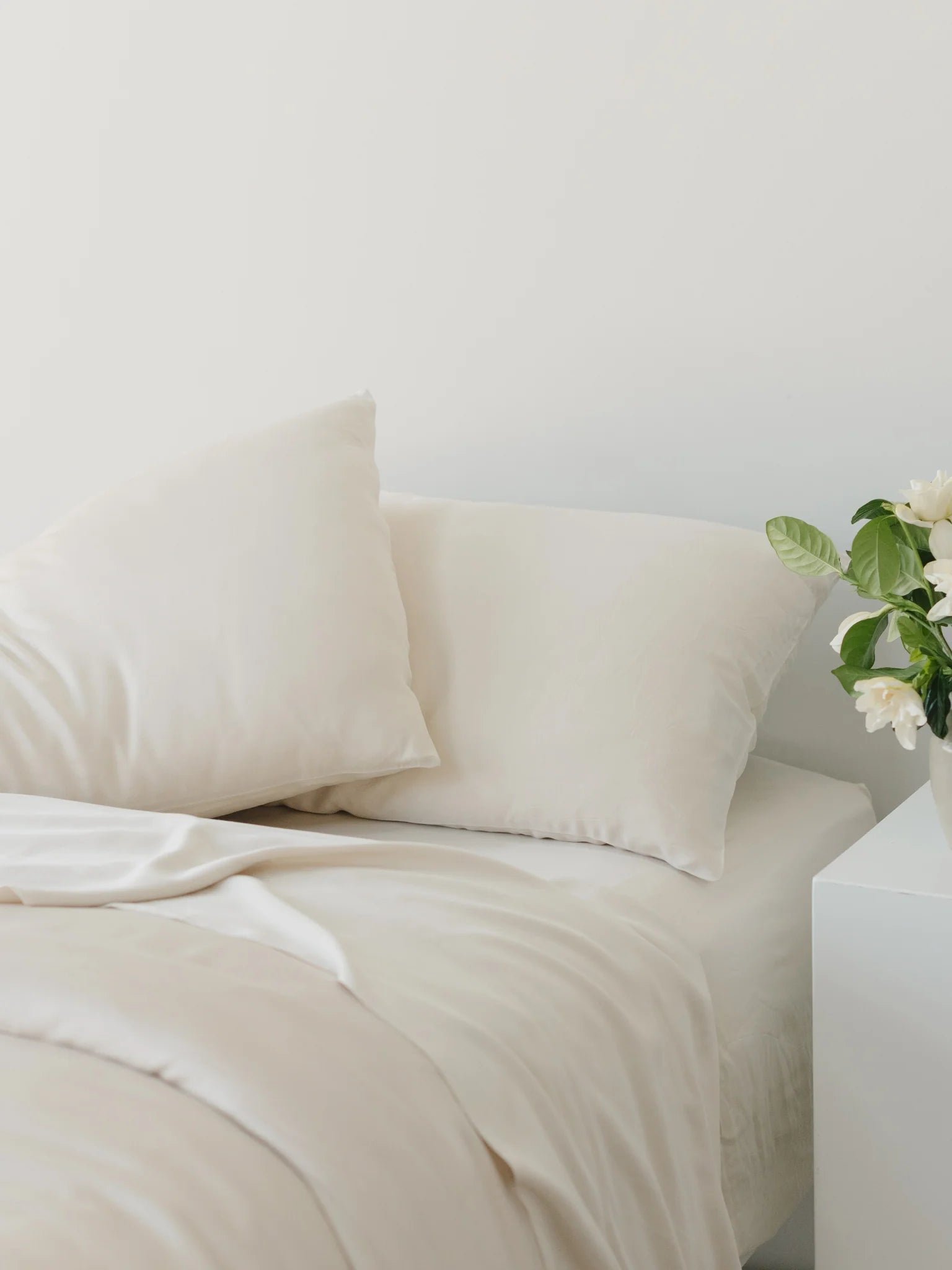 Beige pillows and bedding with white flowers on a nightstand.