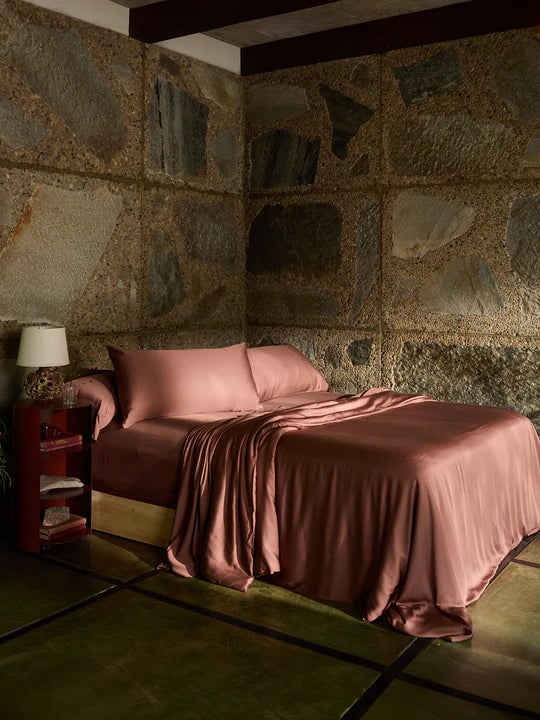 Cozy bedroom with stone walls and pink bedding on a wooden bed frame.
