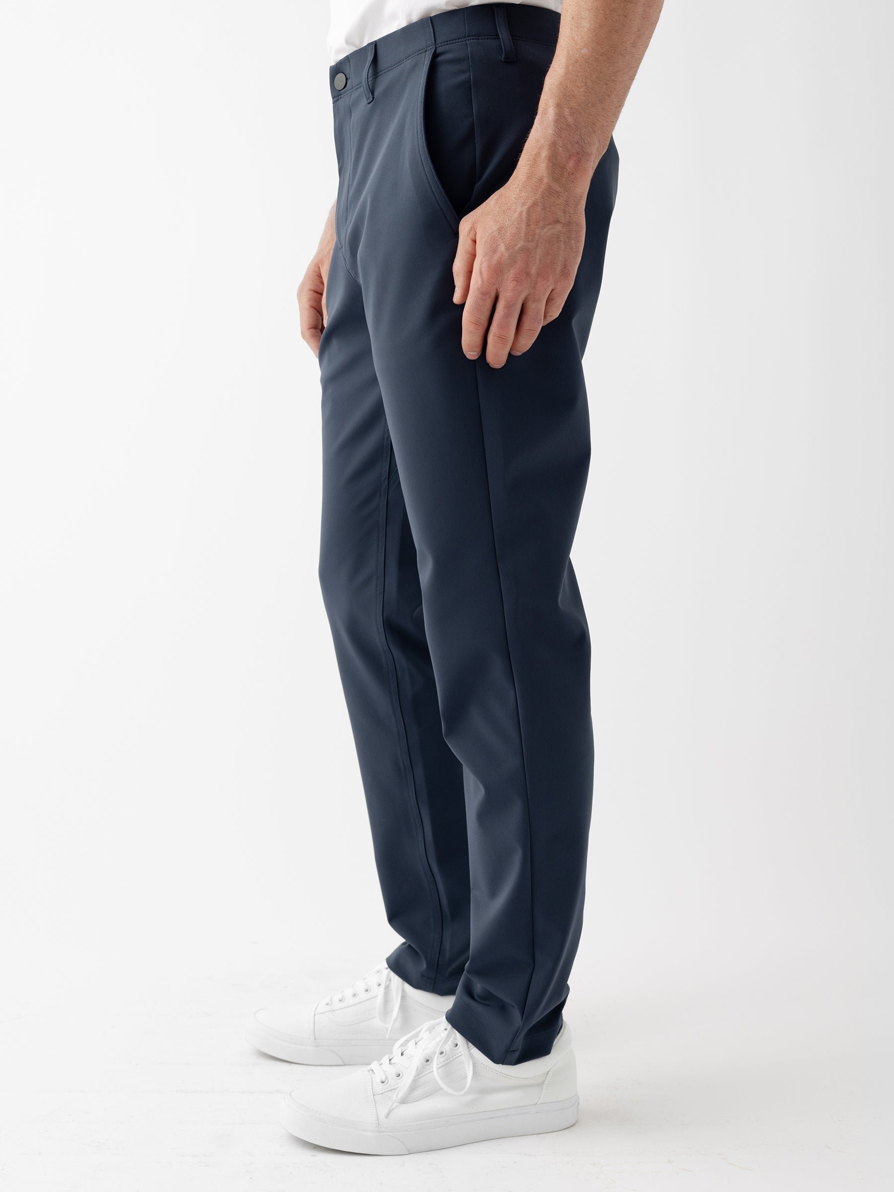 Man wearing navy trousers, white shirt, and white sneakers, standing side view.