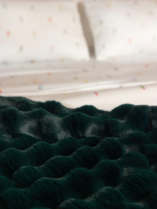 Dark green textured bedspread on a bed with white patterned pillows.