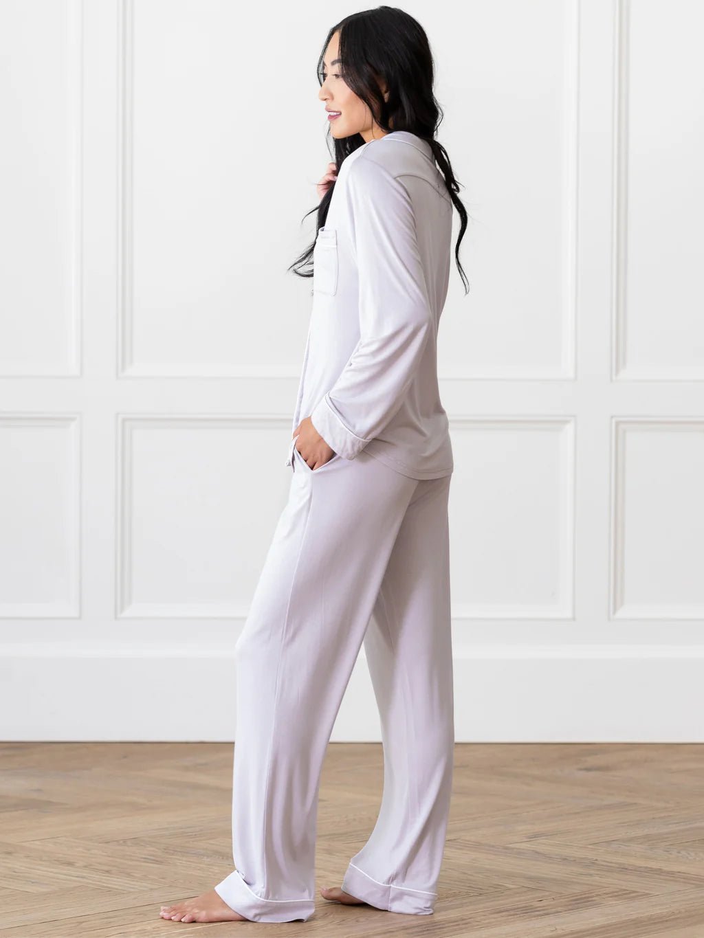 Person wearing white pajamas, standing sideways in a room with wooden flooring and a white paneled wall.