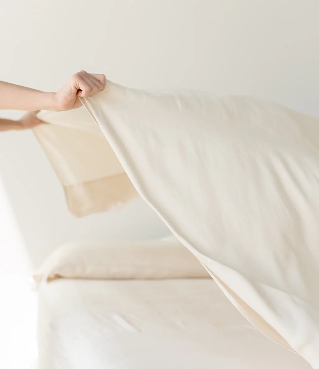 Person making a bed with a beige sheet.