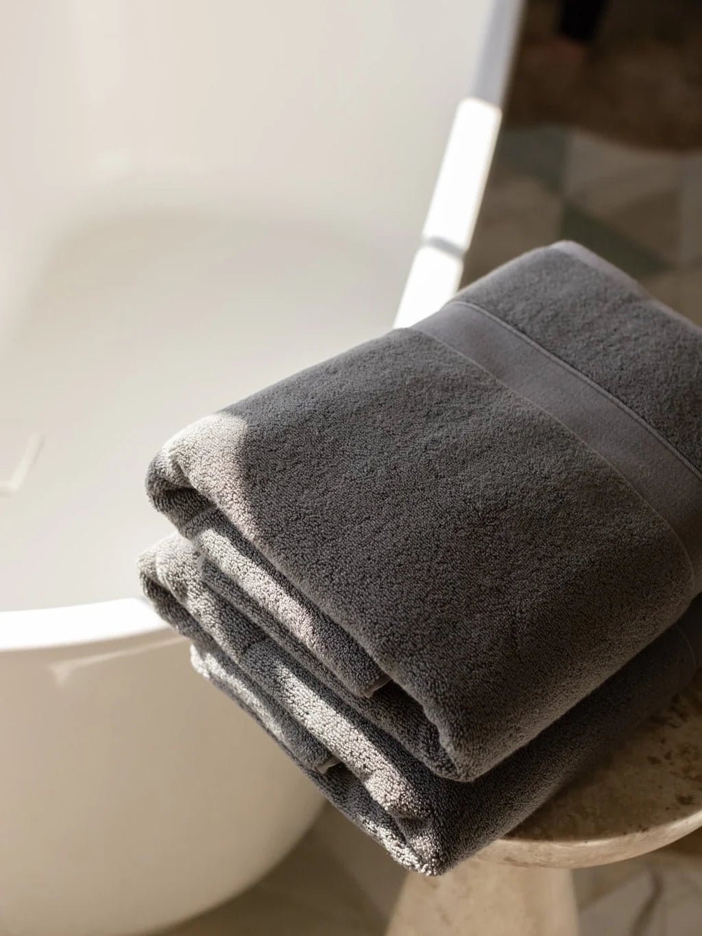Person in a white bathrobe sitting in a modern bathroom near a tub.