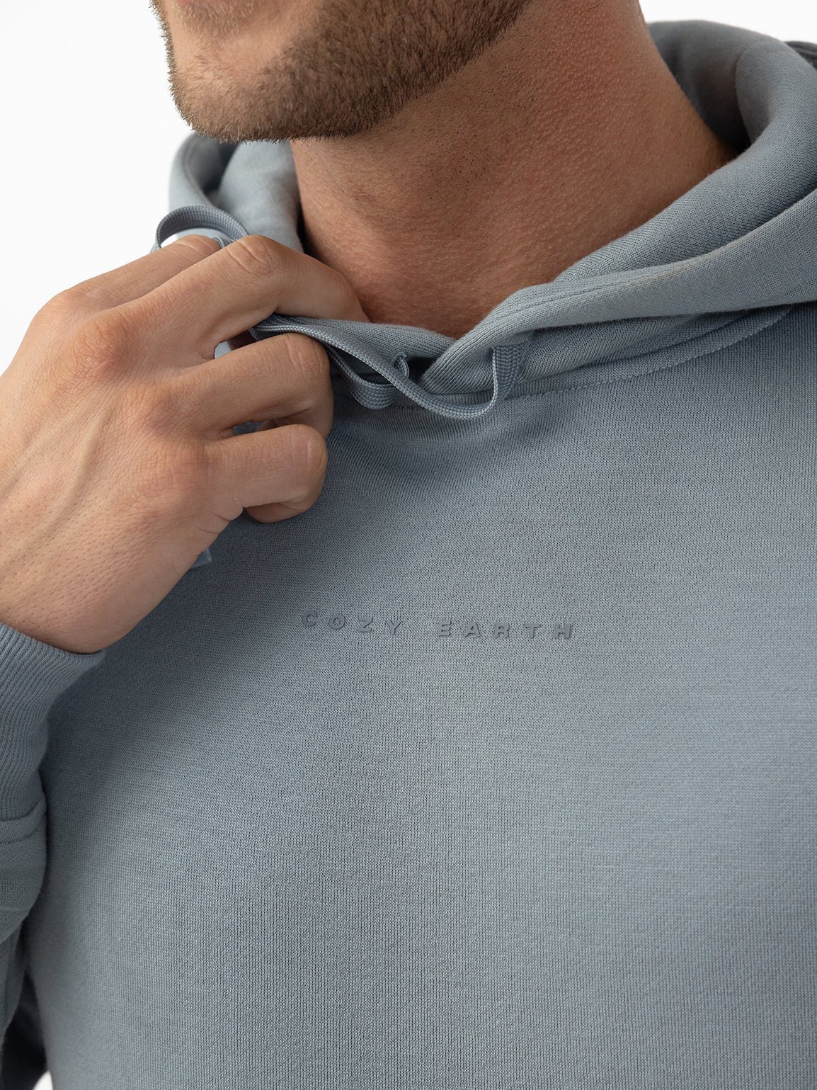Close-up of a person wearing a light blue hoodie with the words 'COZY EARTH' embossed.