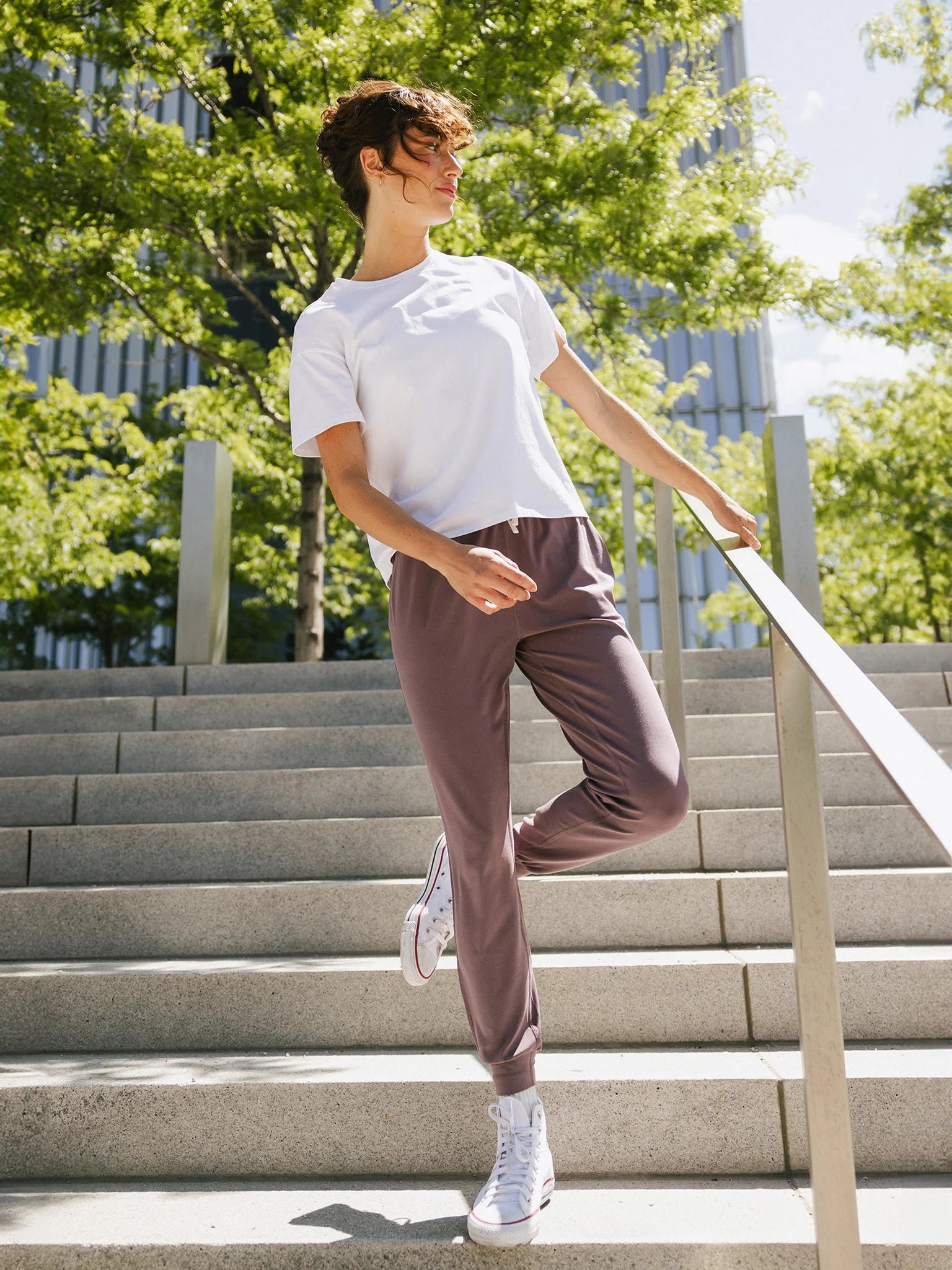 Person in casual attire standing on outdoor stairs under bright sunlight.