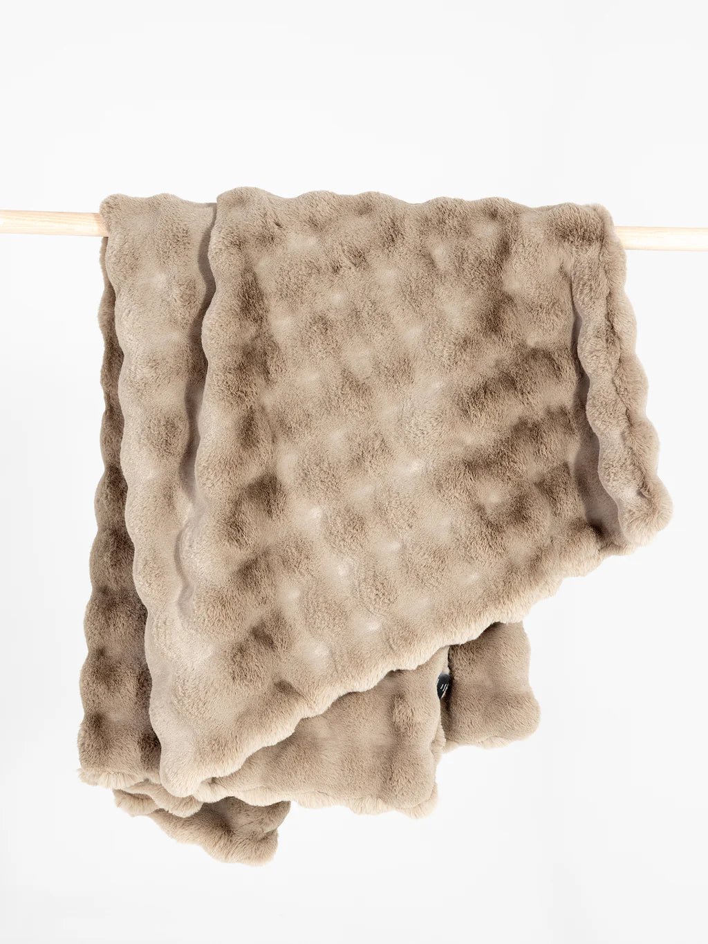 Soft, beige fur blanket hanging over a wooden rod.