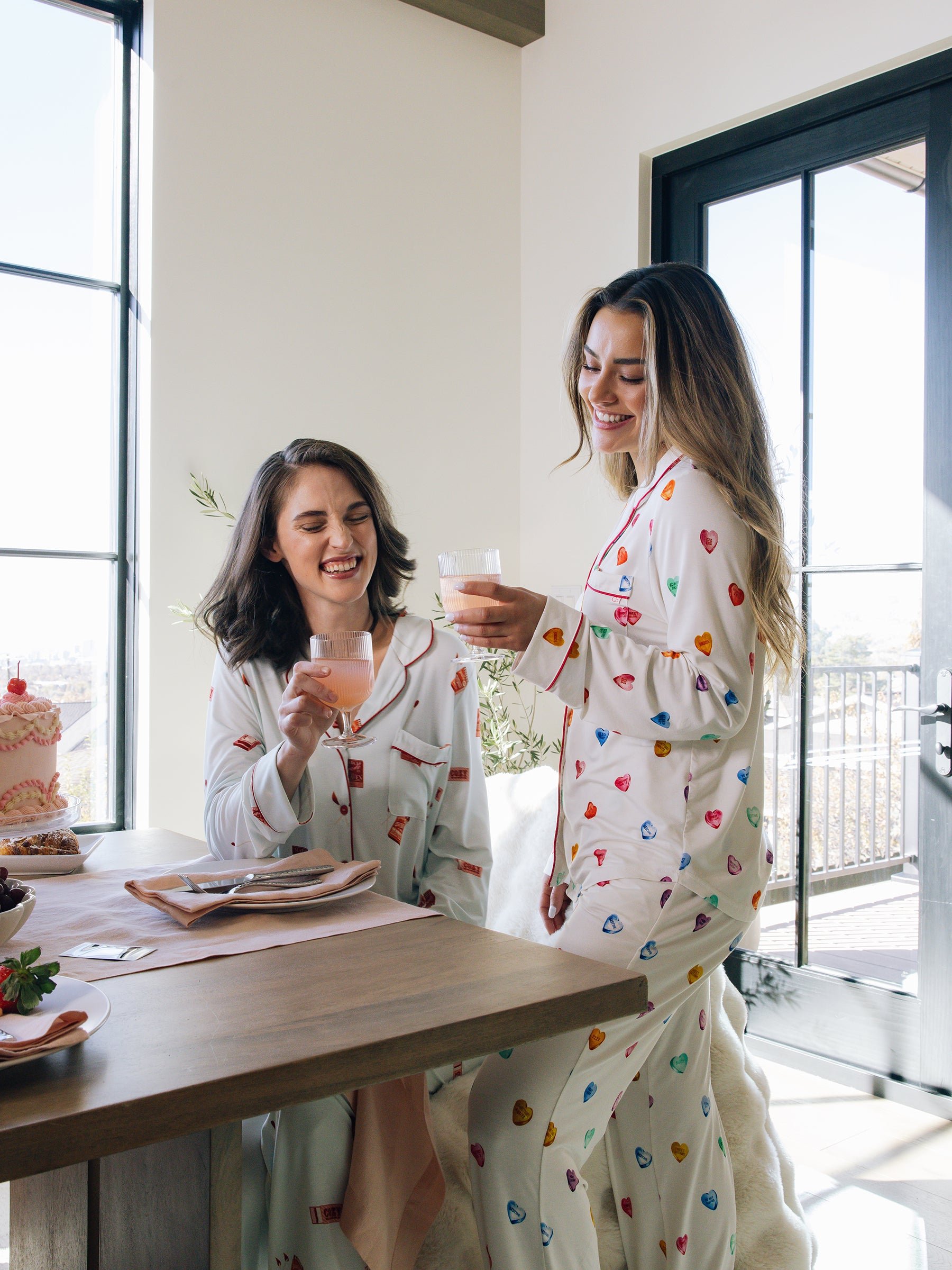 Two people in heart-patterned pajamas enjoying drinks at a dining table.