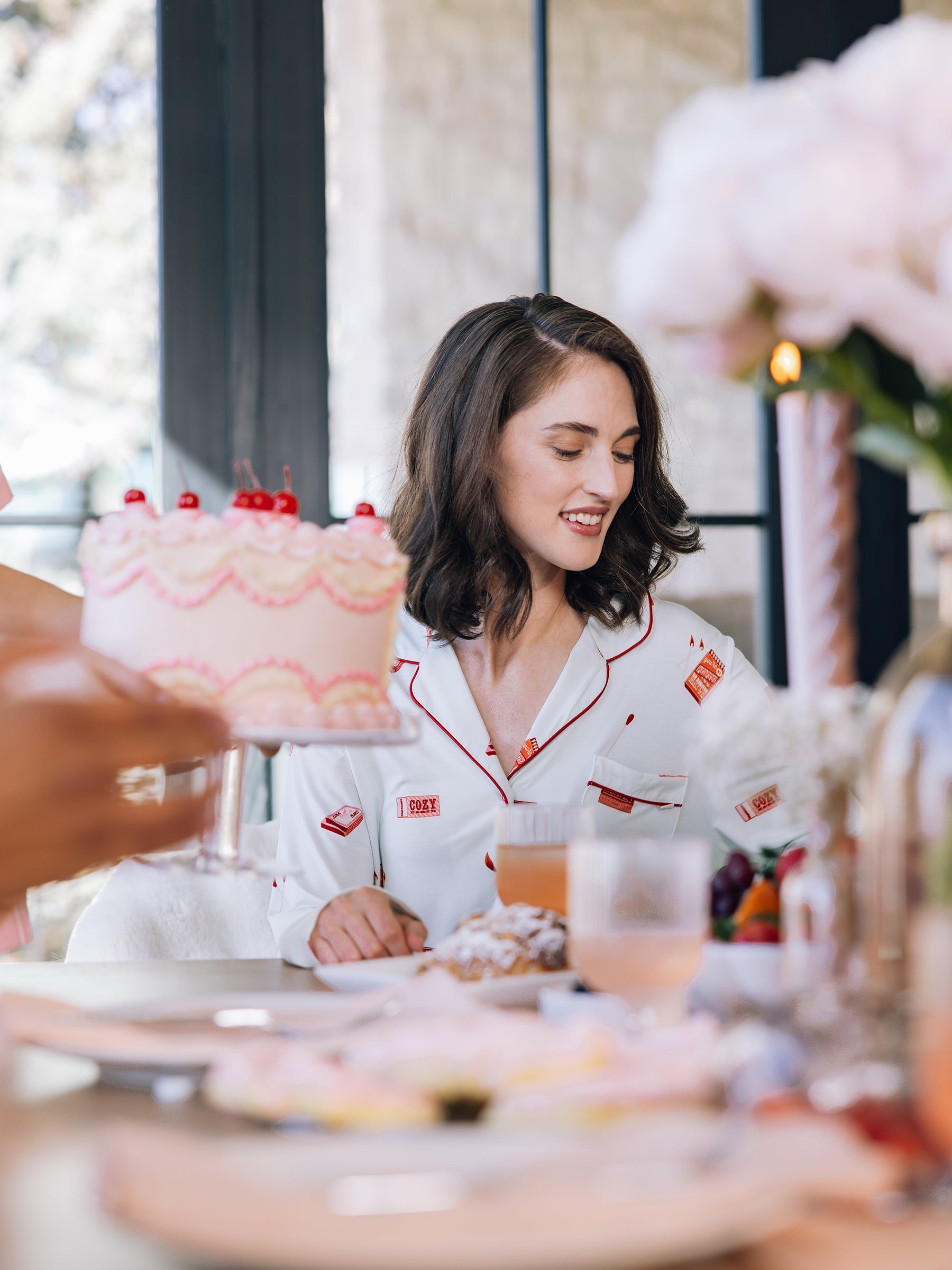 Woman in pajamas sitting at a table with a cake and drinks.