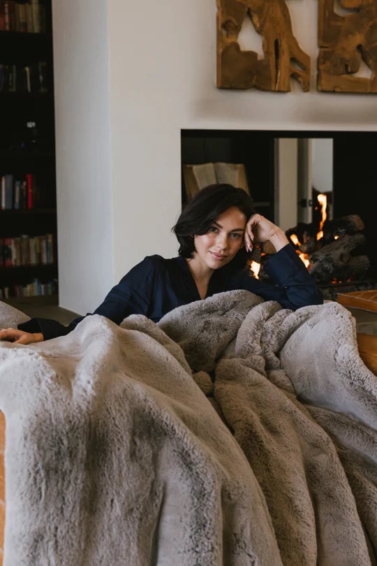 Person relaxing on a couch with a cozy blanket by a fireplace.