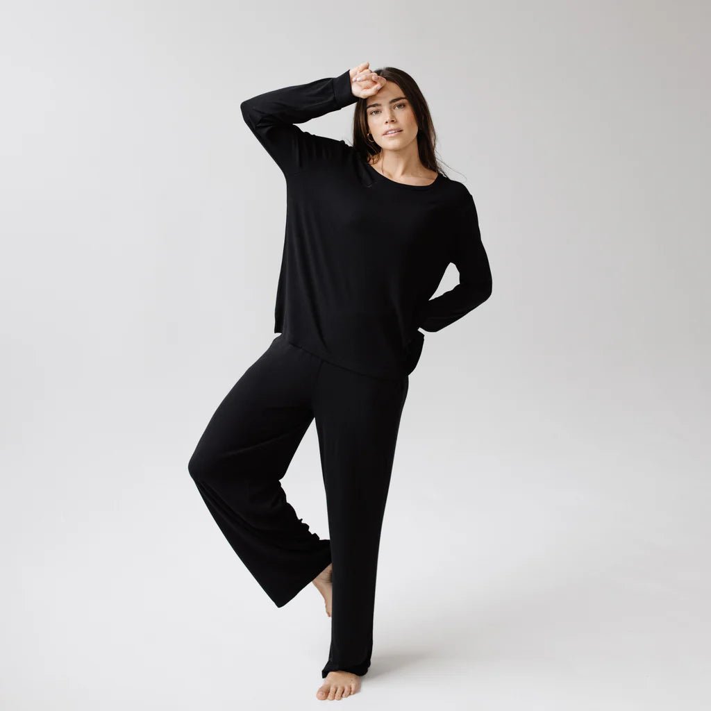 Woman in black loungewear striking a casual pose against a neutral background.