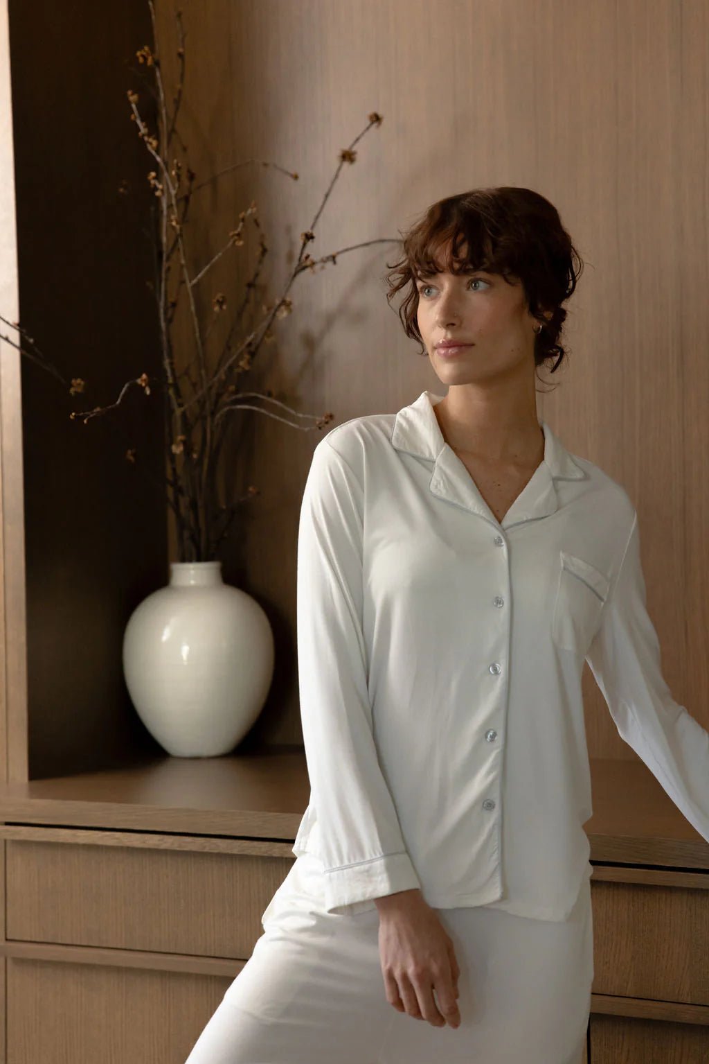 Person in white pajamas standing next to a vase on a wooden cabinet.