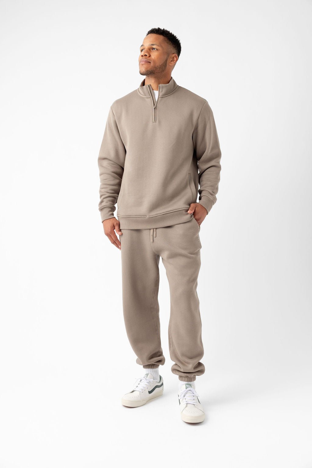 Man in a beige tracksuit with a half-zip sweatshirt and joggers, posing against a plain background.