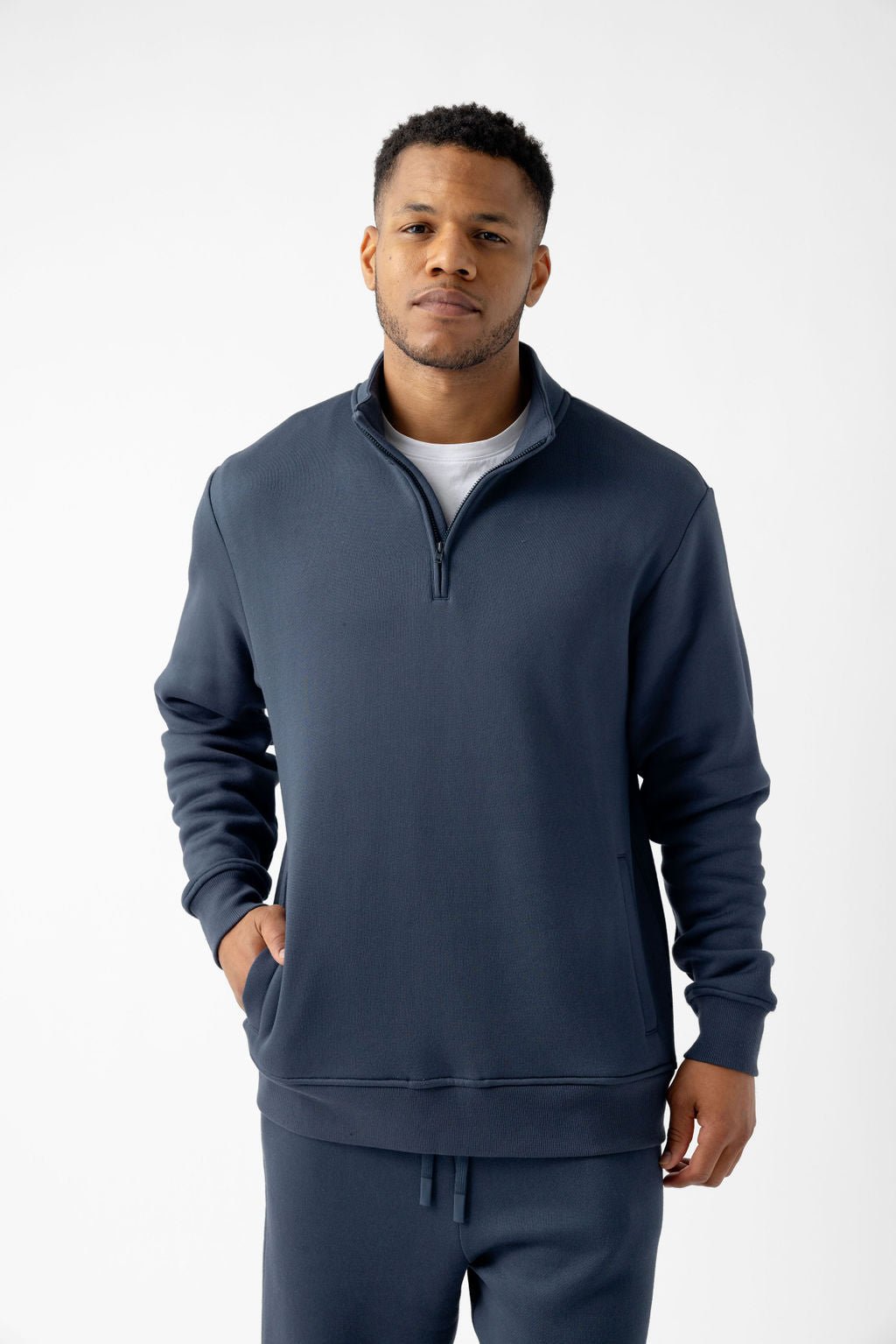 Man wearing a navy quarter-zip pullover with hands in pockets, against a plain background.