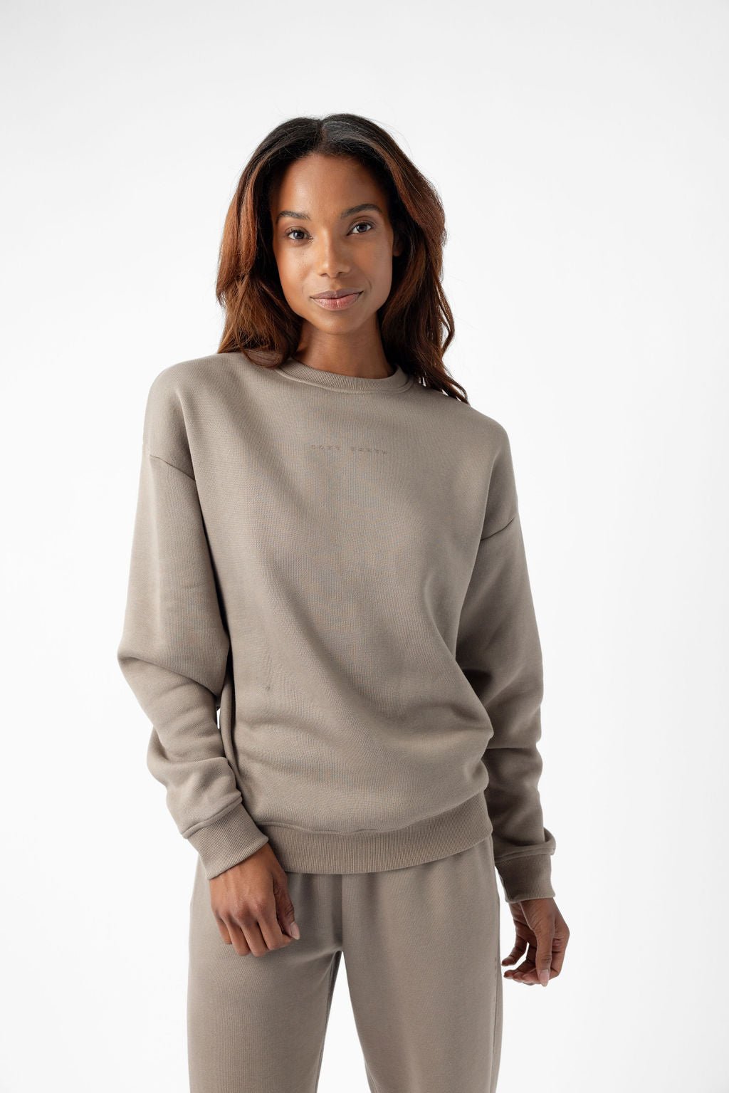 Person wearing a beige sweater and matching pants, posing in a studio setting.